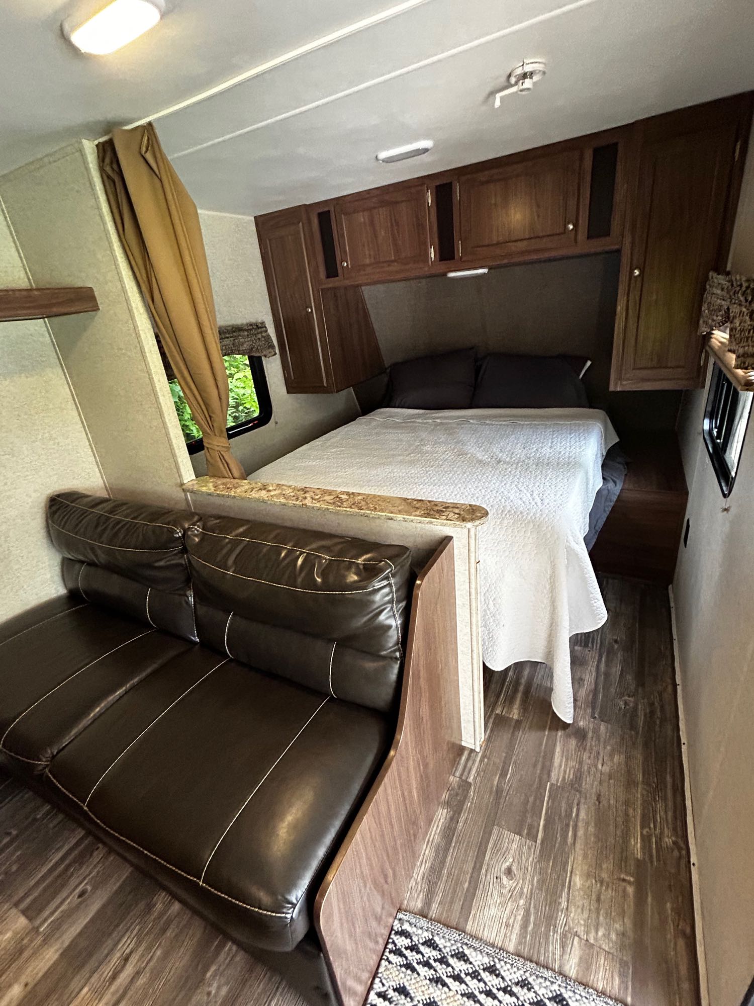 This RV rental interior features a cozy bed, dark leather couch, and wooden cabinetry, perfect for road trips.. Heartland RVs Pioneer 2016