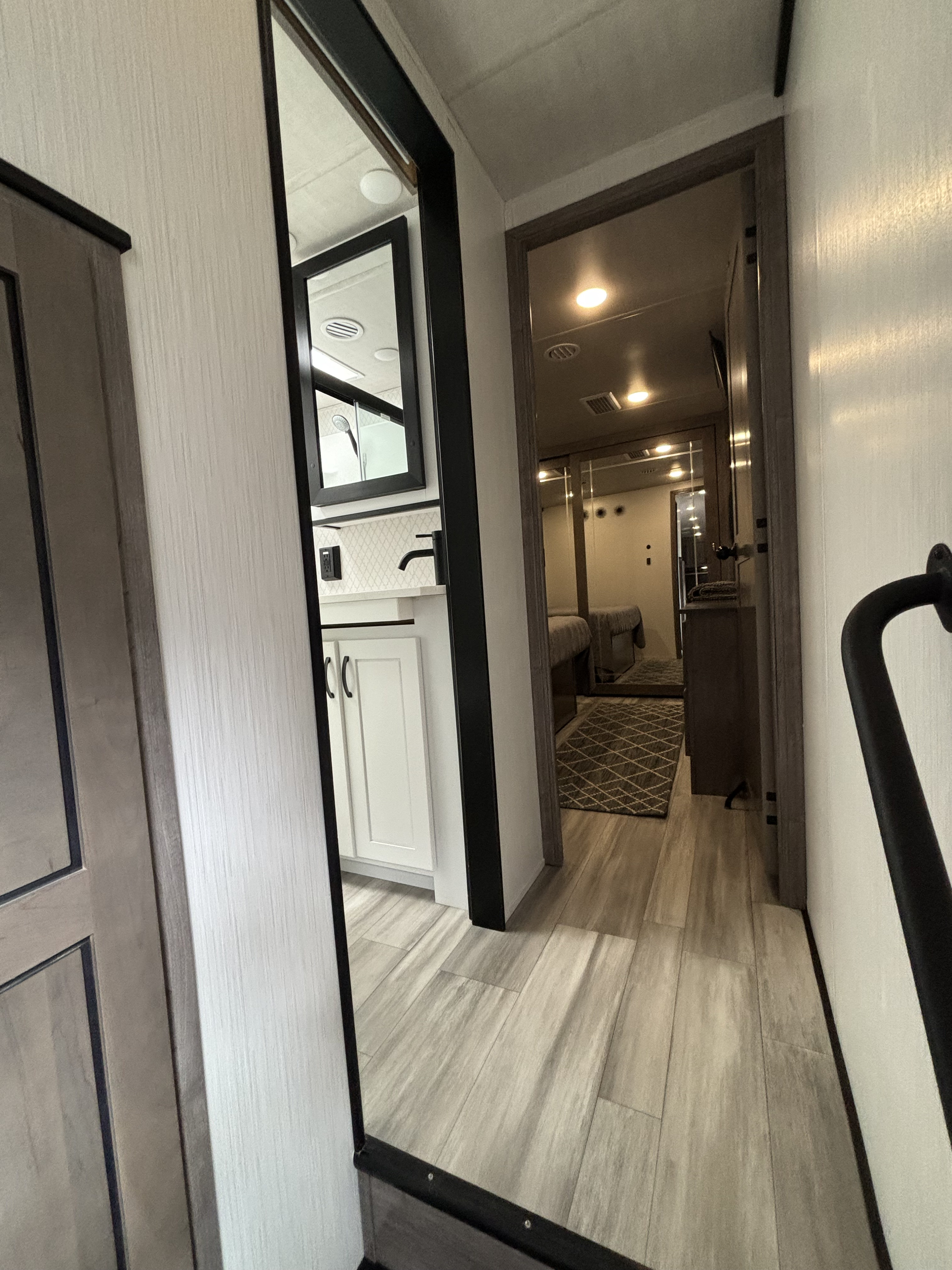 Modern RV rental interior: hallway view showing a bedroom ahead and a bathroom vanity reflected on the left.. Forest River Cedar Creek 311 RL 2022
