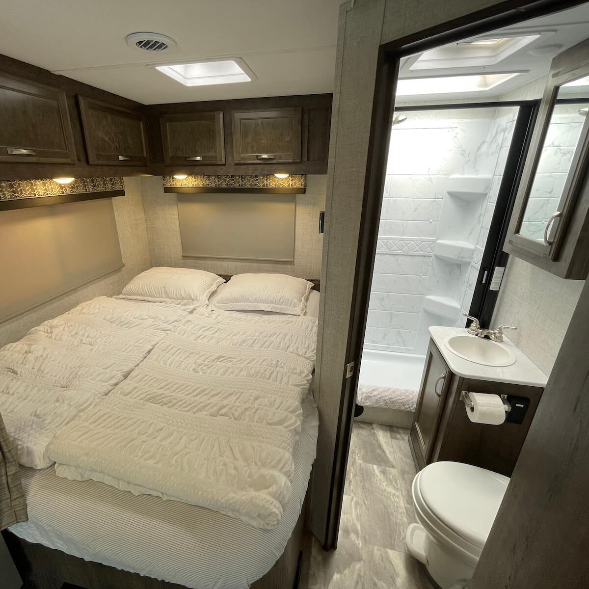 Compact RV rental interior showing a cozy bedroom and an adjacent bathroom with shower, sink, and toilet.. Gulf Stream Conquest 2022