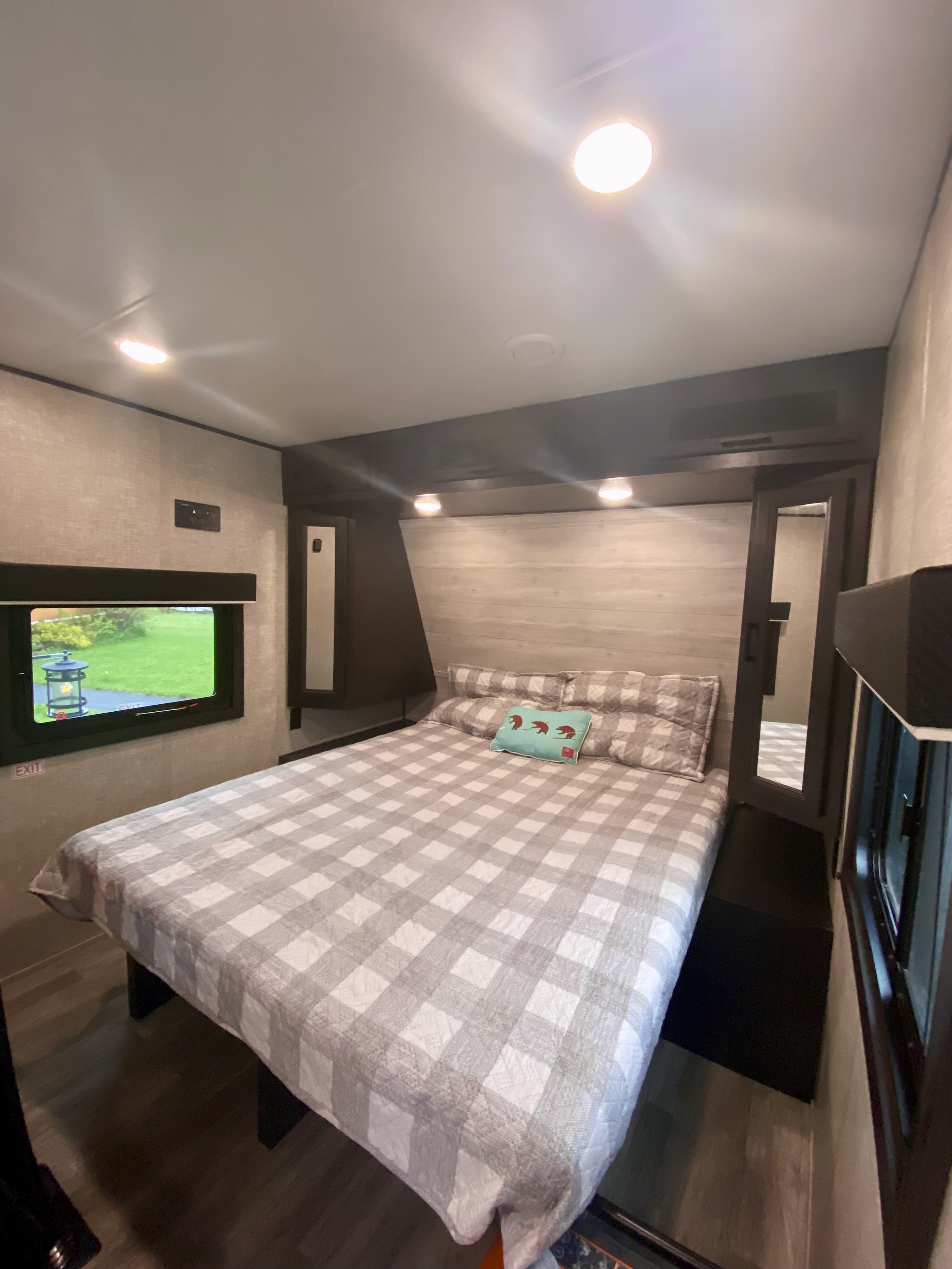 A clean and modern rv rental bedroom featuring a large bed with a plaid comforter, side mirror, and window view.. Jayco Jay Flight 2022