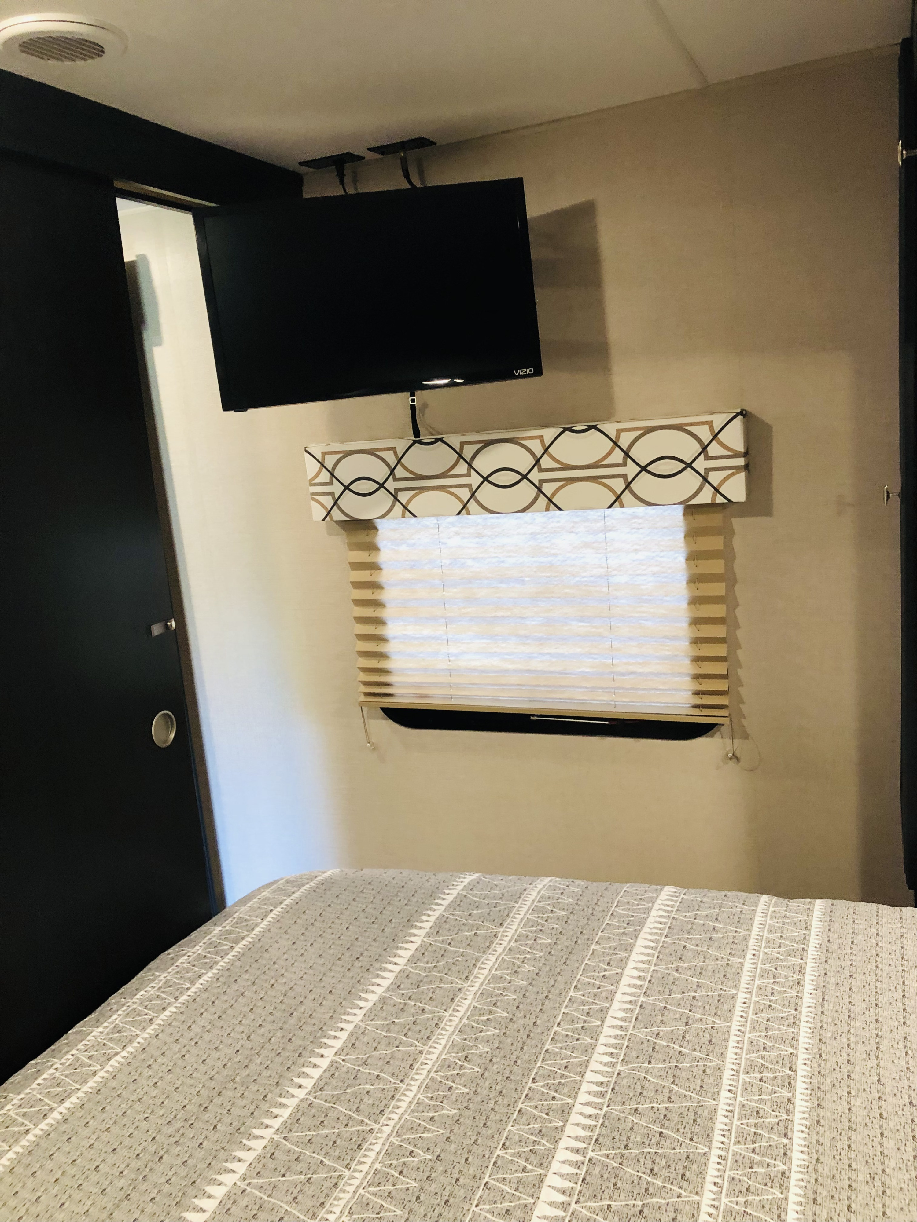 RV rental bedroom with TV, window with blinds, and patterned bedding. A cozy and functional compact space.. Sport Trek Sport Trek Trailer 2019