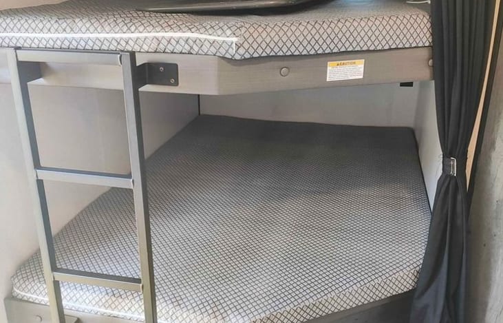 Inside an RV rental, two patterned bunk beds offer sleeping space, with a ladder for access and privacy curtains.. Keystone RV Hideout 2022