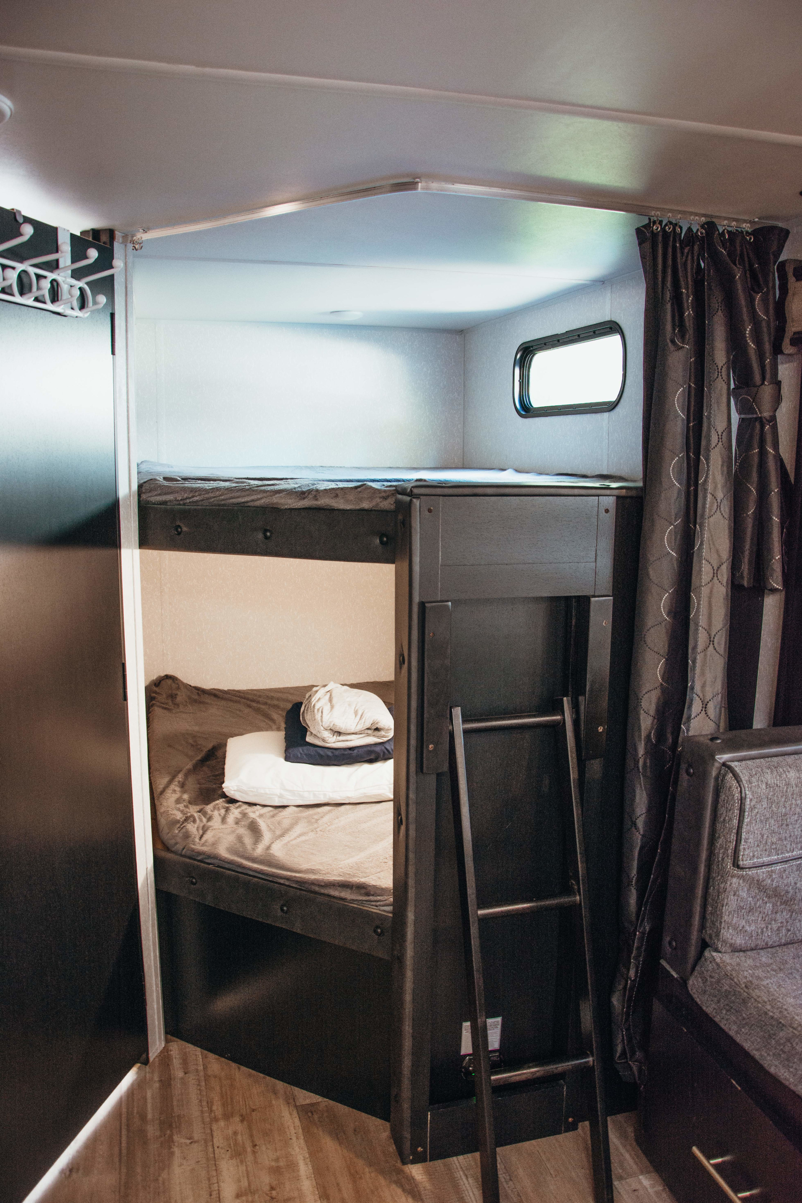 RV rental interior: practical bunk beds with a ladder, window, and bedding for comfortable travel.. Forest River Cherokee Grey Wolf 2022