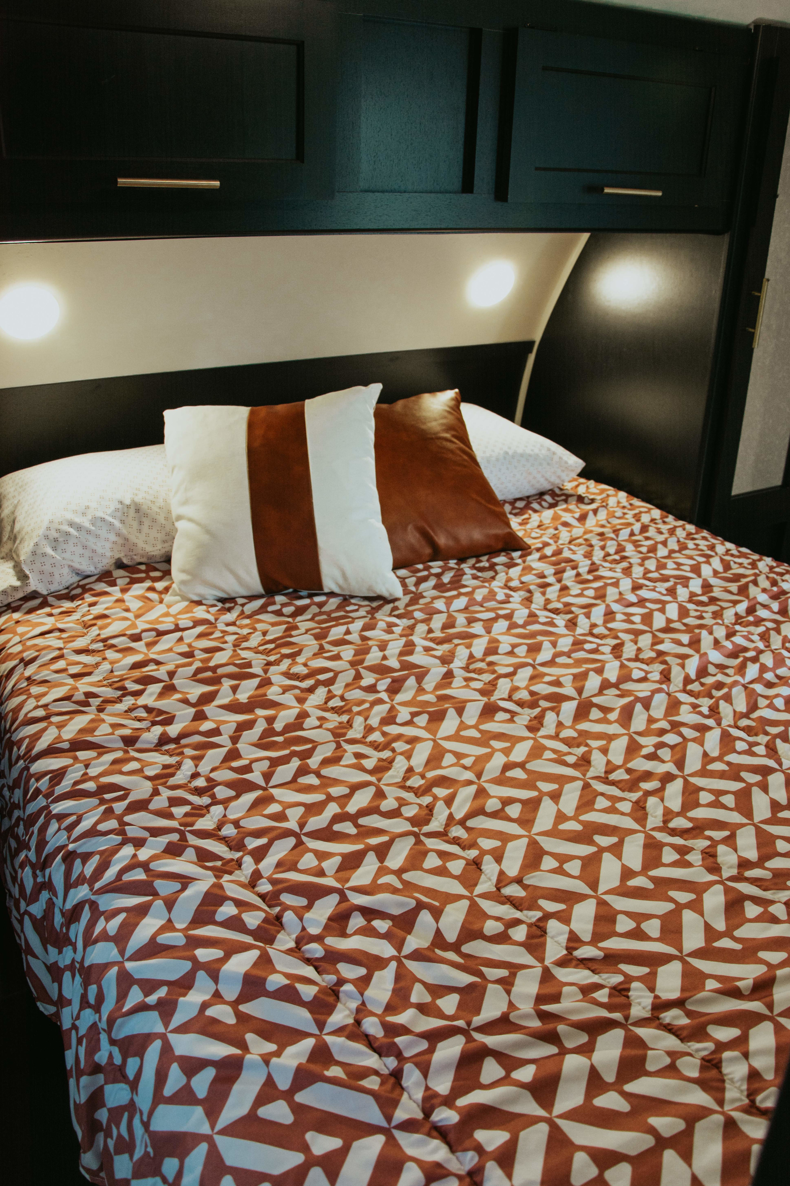 Cozy RV rental bedroom featuring a bed with a geometric patterned comforter, decorative pillows, and overhead cabinets with lights.. Forest River Cherokee Grey Wolf 2022