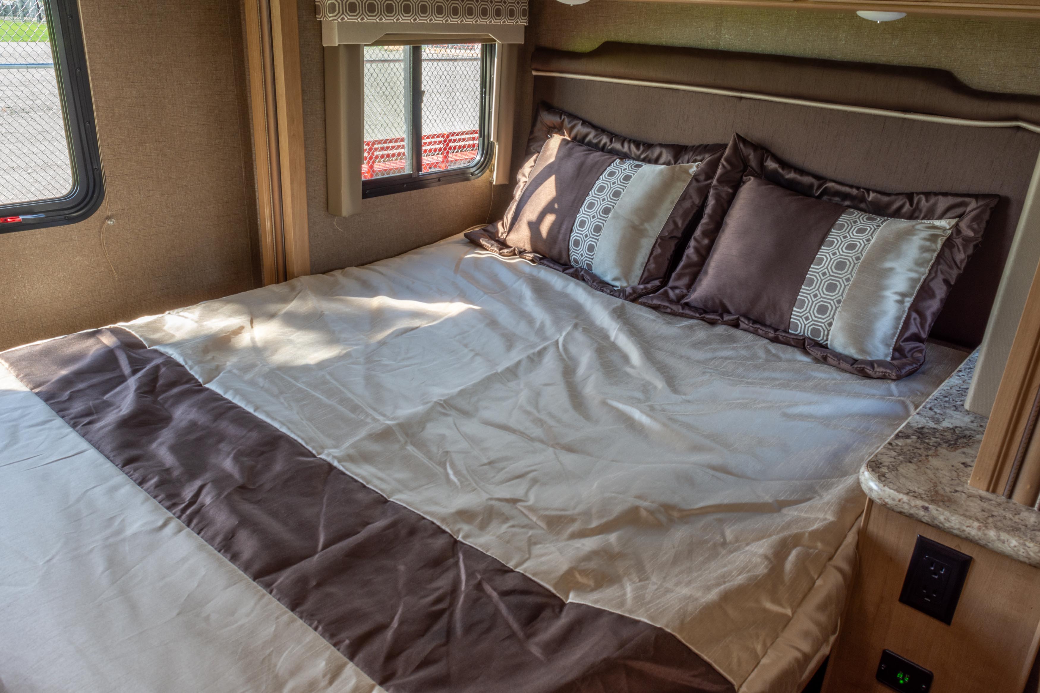 Comfortable RV rental bedroom featuring a brown and cream bed with patterned pillows, illuminated by natural light.. Thor Four Winds 2019