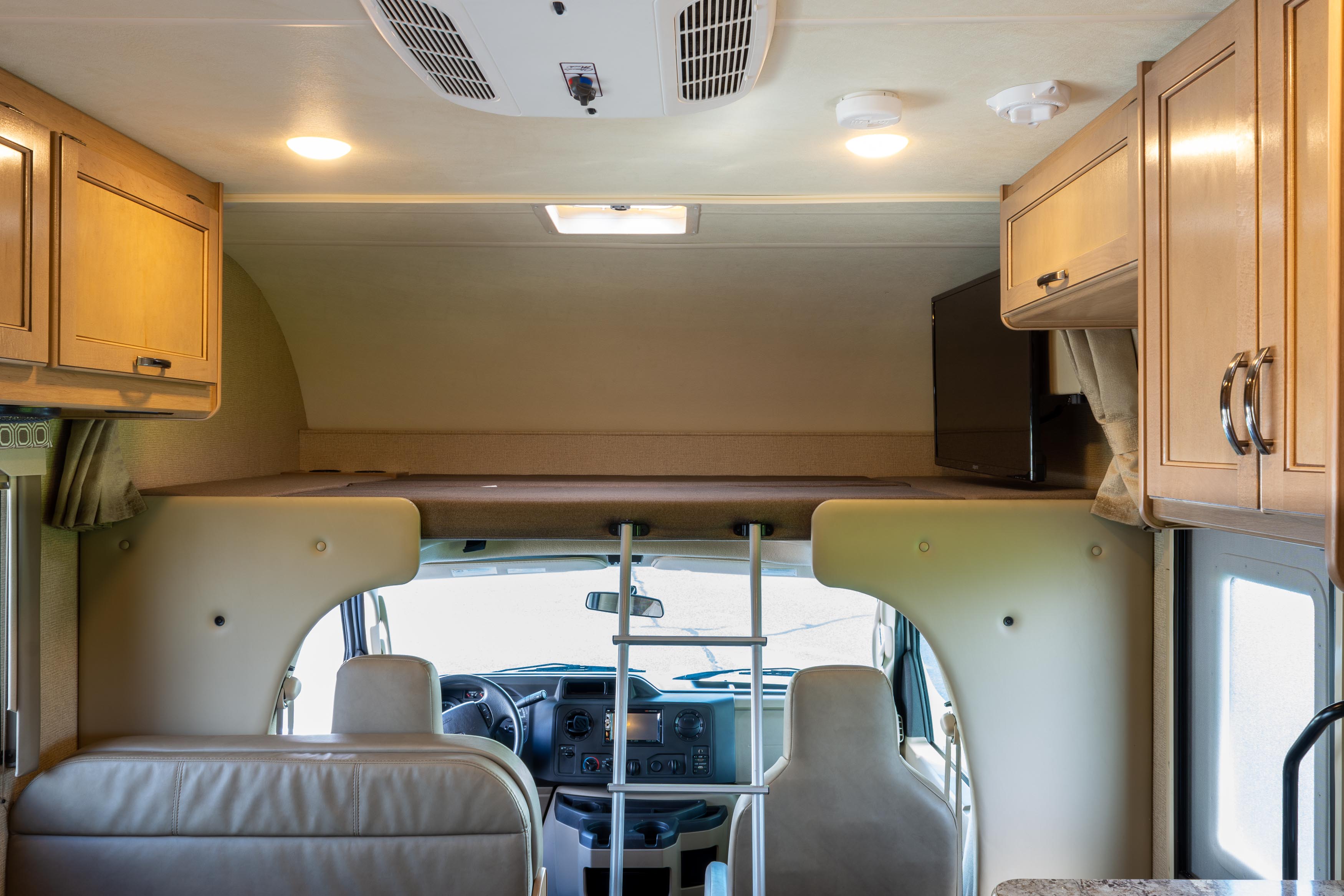 Inside an RV rental, featuring the overhead bunk with ladder access, front seats, and dashboard for road trips.. Thor Four Winds 2019