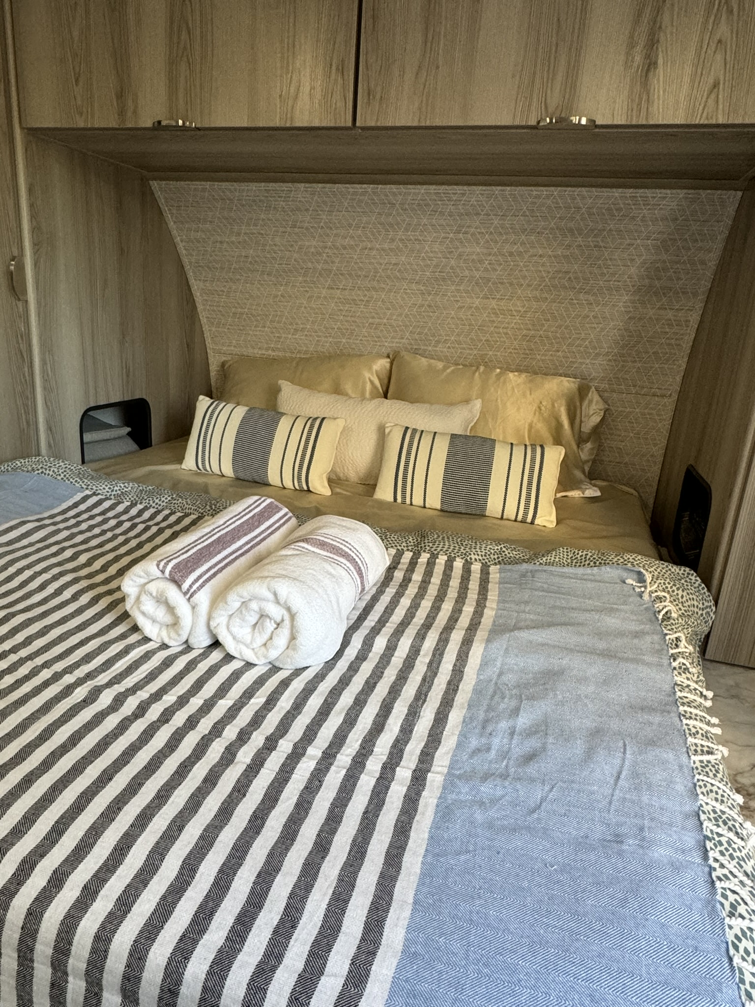 Cozy RV rental bedroom features a striped bedspread, rolled towels, and compact storage nooks.. Forest River Salem 2024