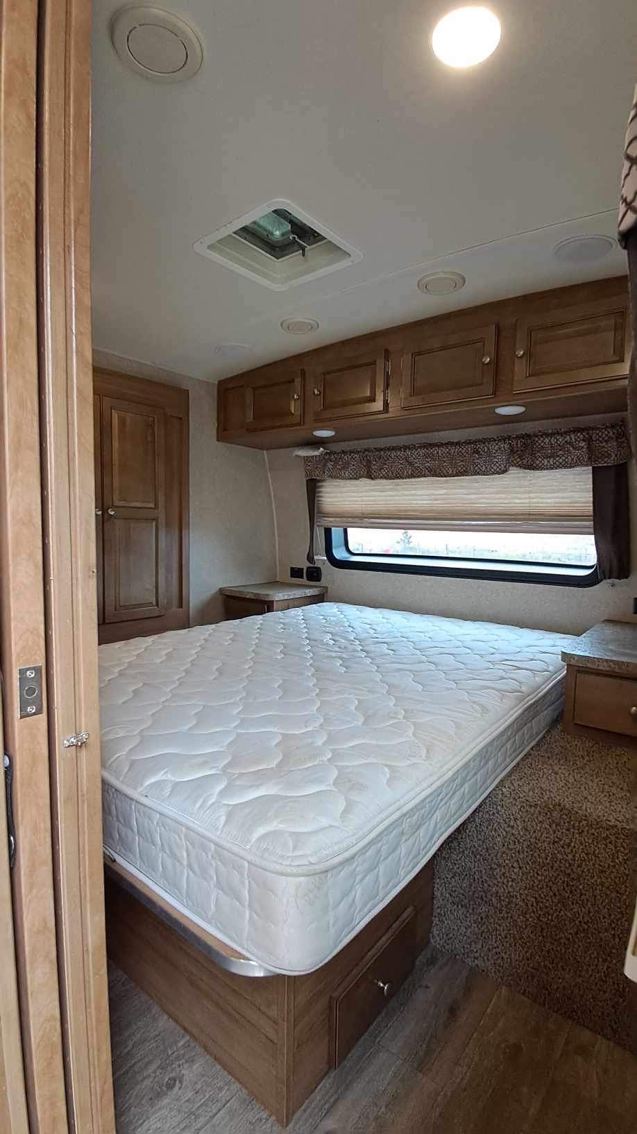 Step inside this cozy RV rental bedroom, featuring a comfy bed, wood cabinets, and a large window.. Forest River Rockwood 2018