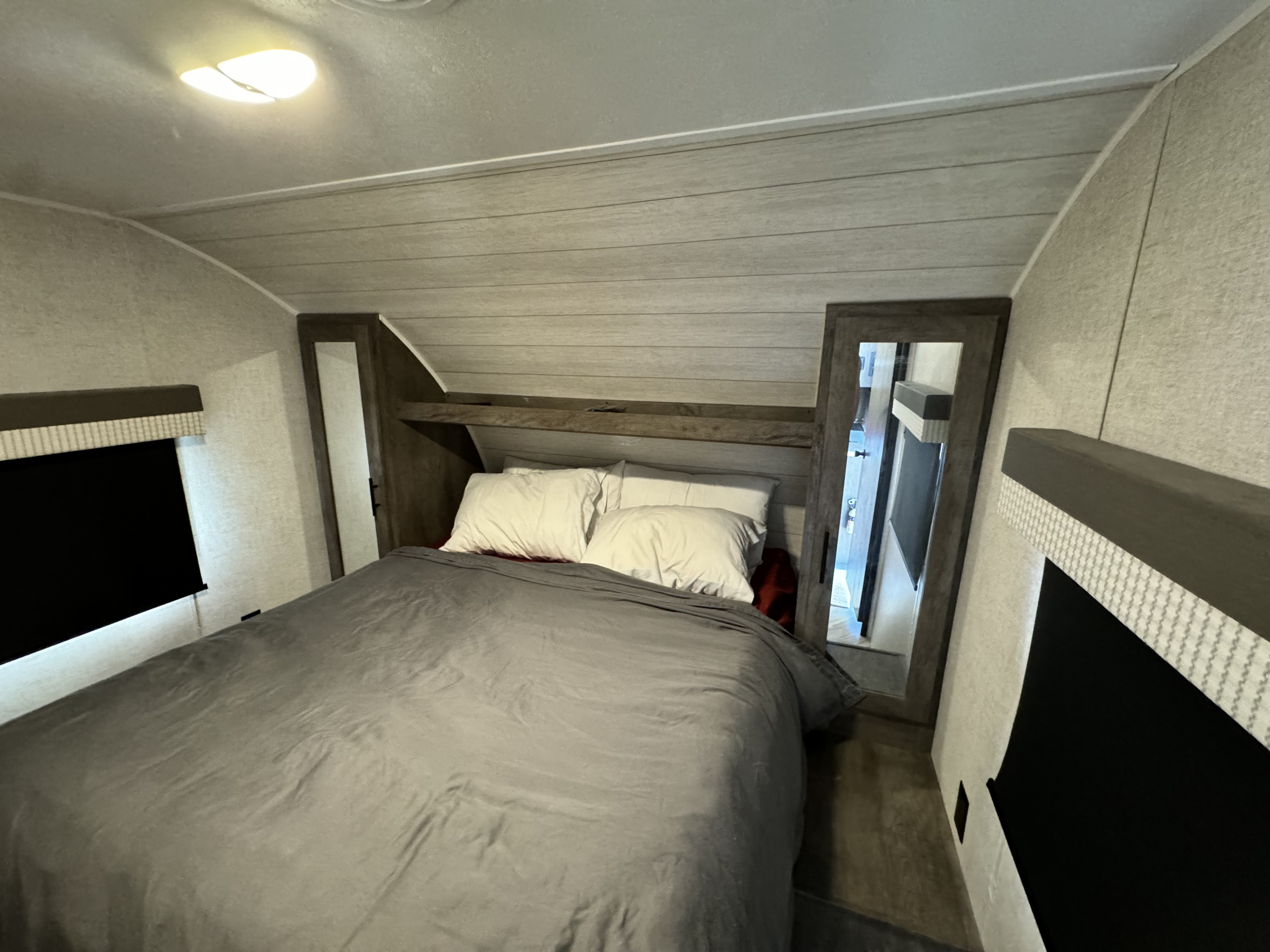 Cozy RV rental bedroom featuring a comfortable bed, built-in storage, and a window with a black shade.. Forest River Wildwood X-Lite 2021