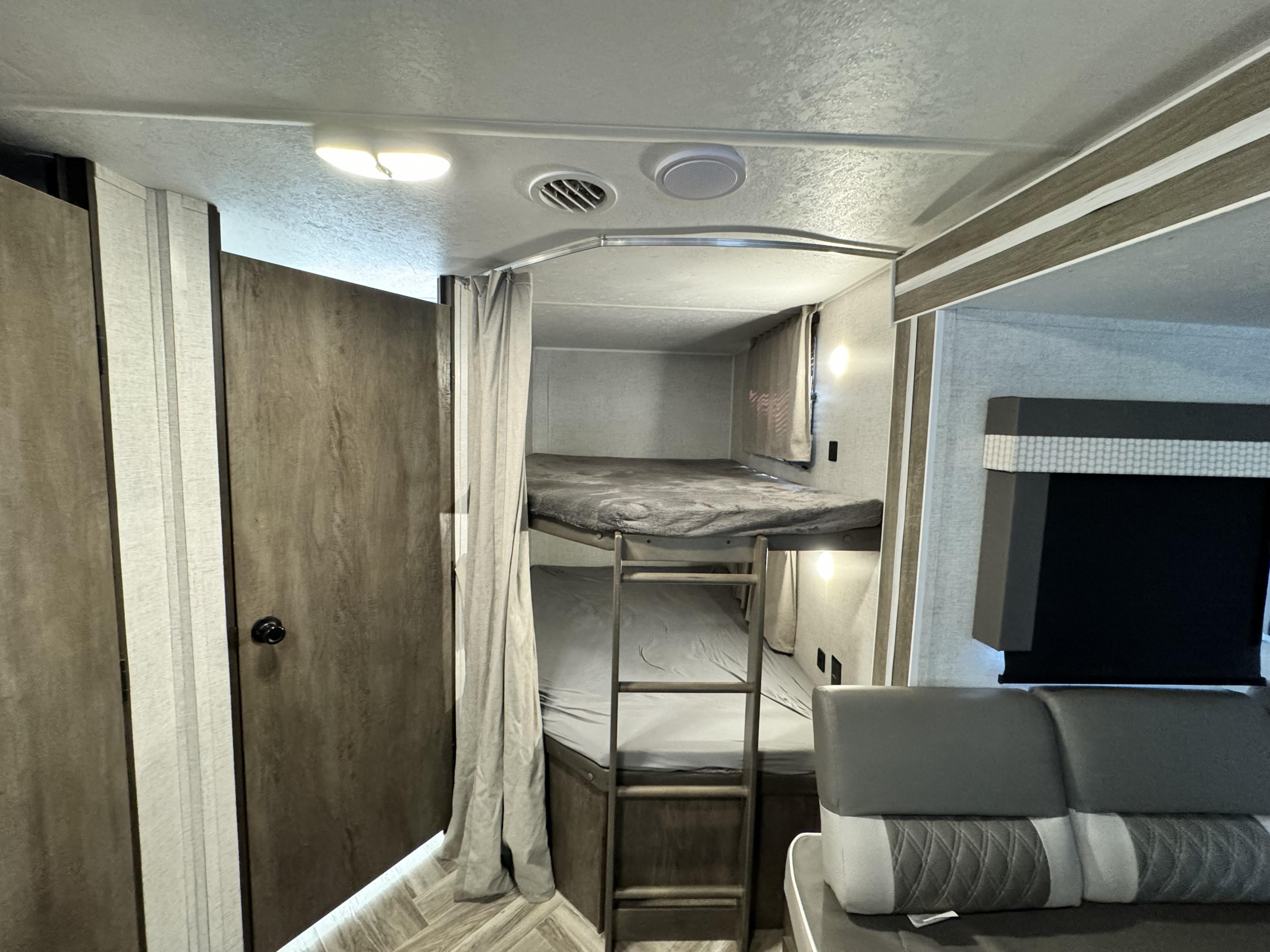 Inside an RV rental: view of stacked bunk beds with a ladder, a light gray privacy curtain, and modern gray seating.. Forest River Wildwood X-Lite 2021