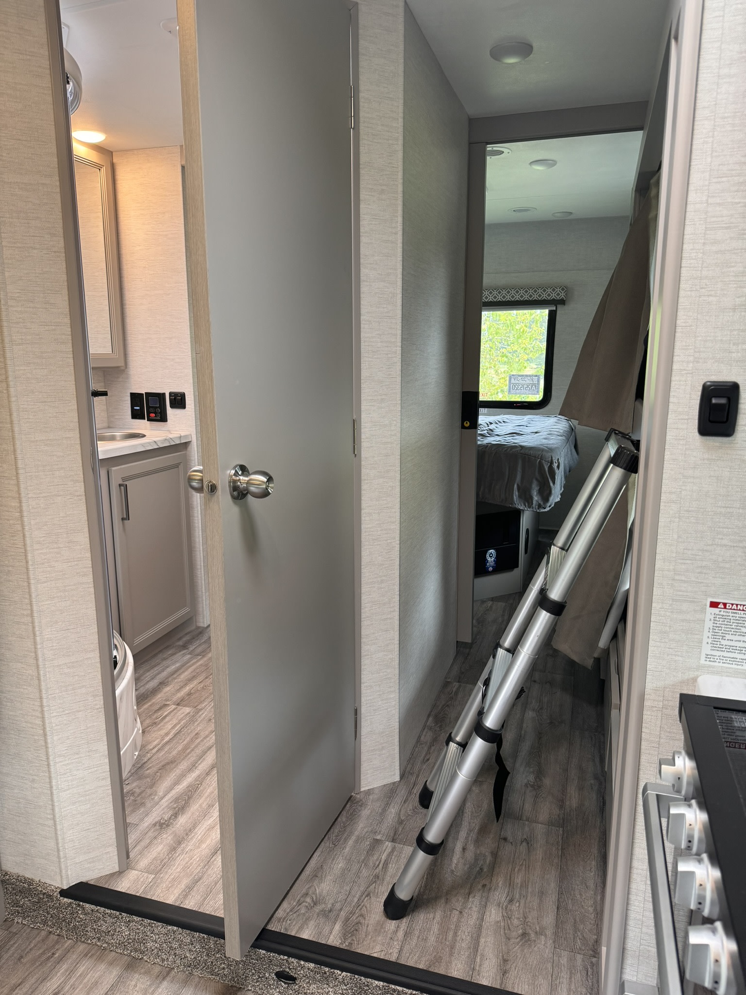 RV rental interior: View of bathroom on left, central door, and bedroom with a bunk bed ladder.. Thor Coleman 2024