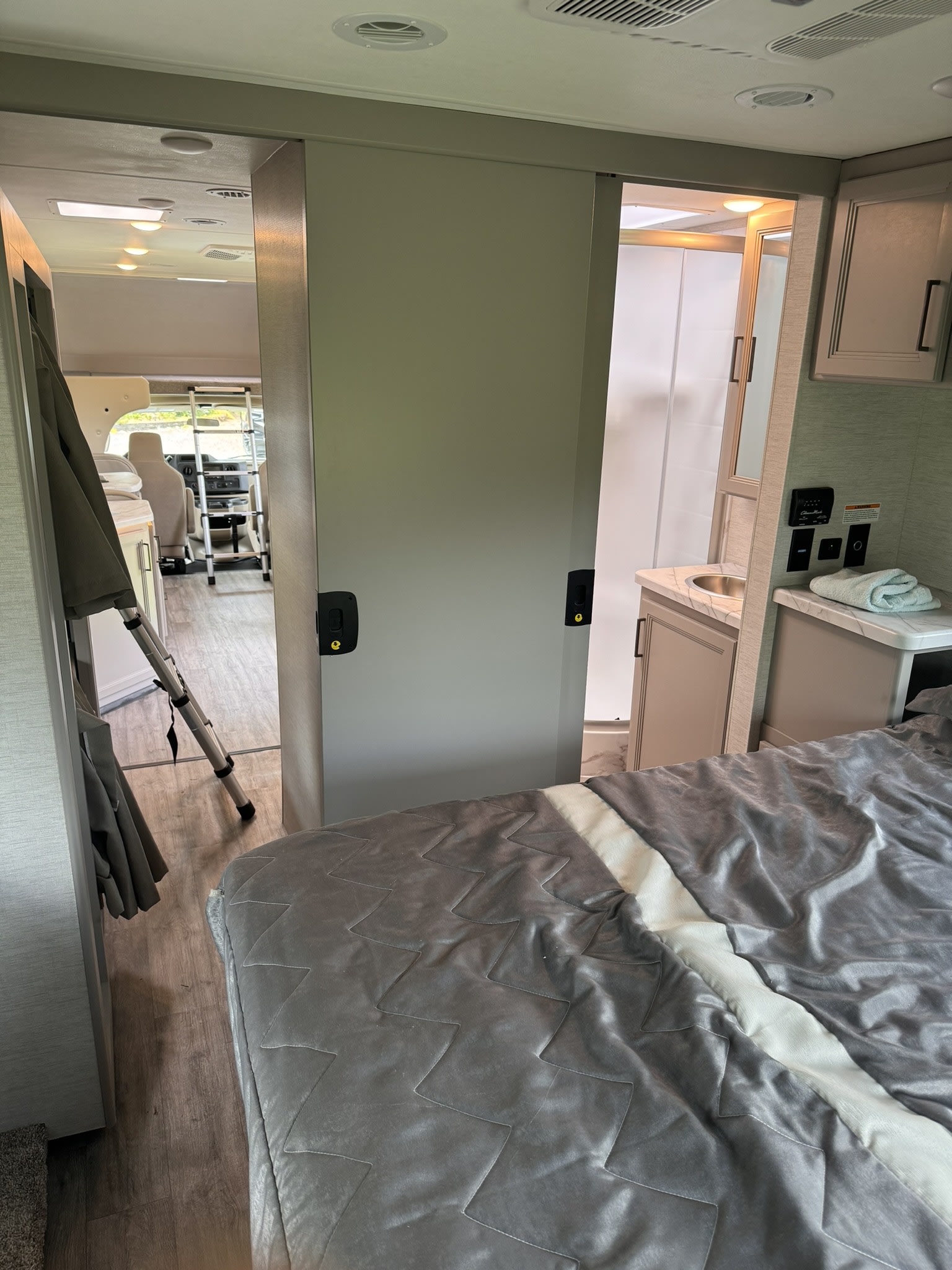 An RV rental's compact interior showing a grey-quilted bed, sliding doors to the bathroom, and forward cabin.. Thor Coleman 2024