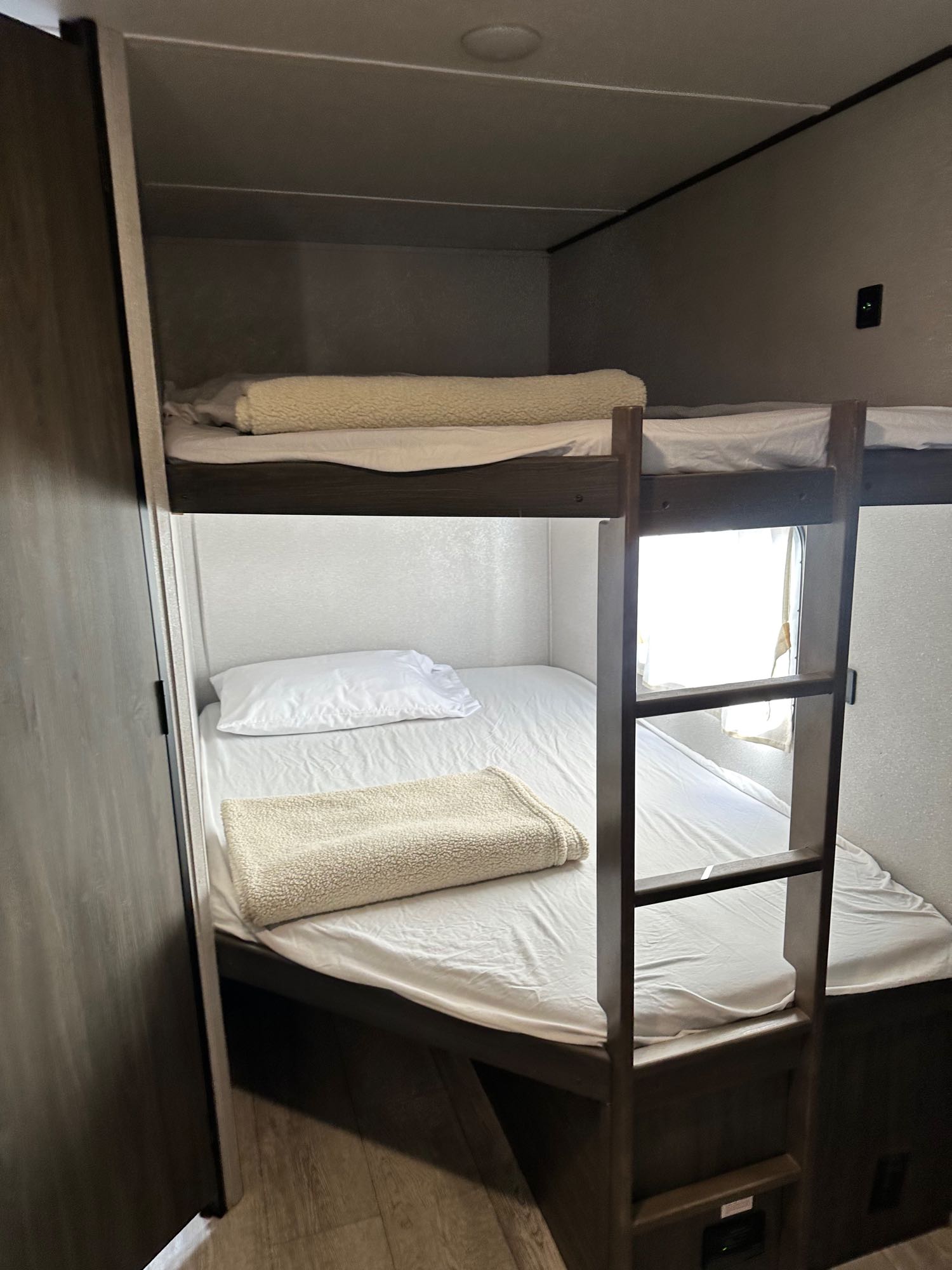 RV rental bunk beds: a cozy sleeping area with white sheets, blankets, a ladder, and a bright window.. Shasta 26db 2021