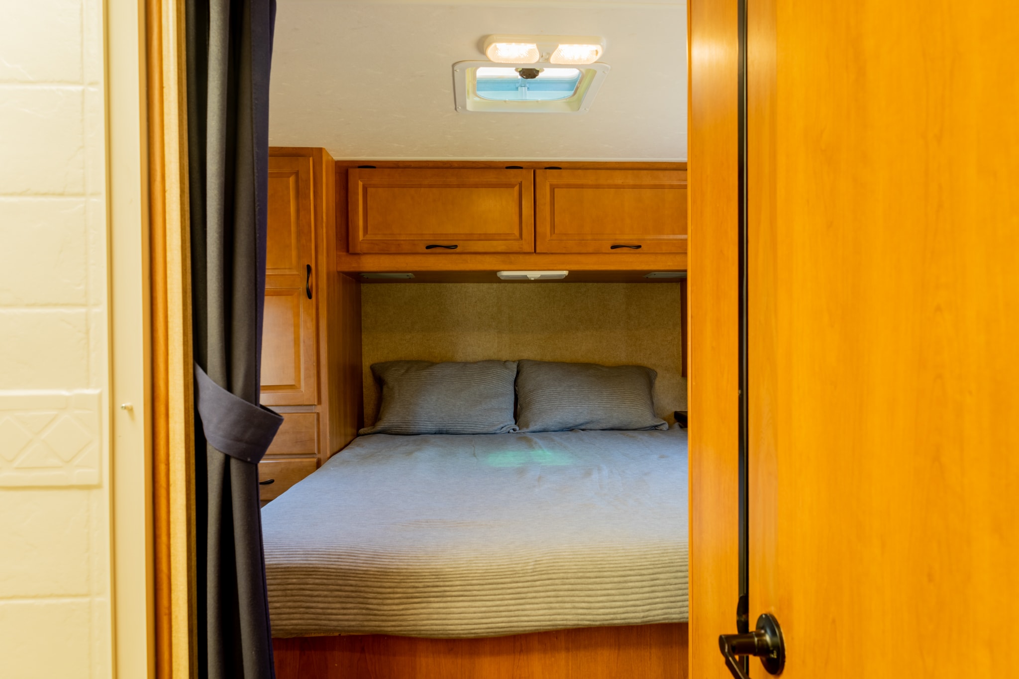 View into a compact RV rental bedroom, featuring a comfy bed with pillows, overhead cabinets, and ceiling lighting.. Thor Majestic 2015