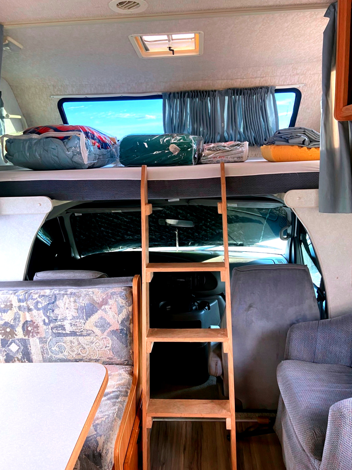 RV rental interior showing a high bunk bed with bedding, a ladder, dinette, and front cabin area.. Winnebago Minnie Winnie 2001