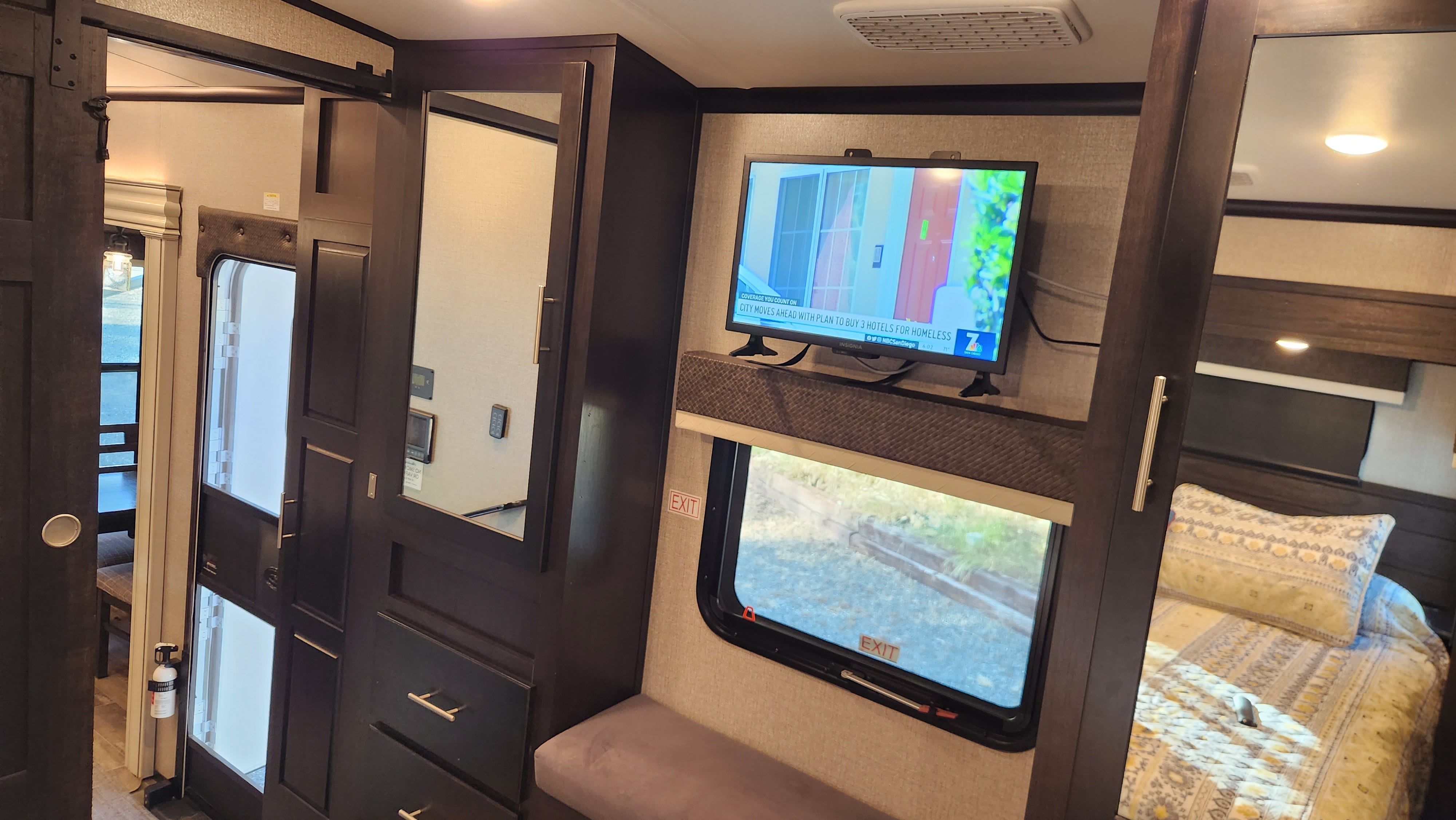 RV rental interior featuring a TV, cozy bedroom, built-in storage with mirror, and window with EXIT sign.. Jayco North Point 2021