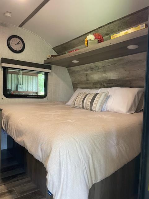 RV rental bedroom: a comfortable bed with pillows, overhead shelf, window, and wall clock. Cozy and well-appointed.. Gulf Stream Ameri-Lite Super Lite 2022