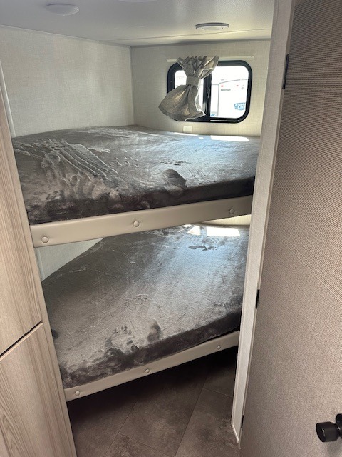 **RV rental** bunk beds: a compact, two-tier sleeping area with grey covers and a window, ideal for extra guests in an RV.. Forest River SALEM FSX 2024