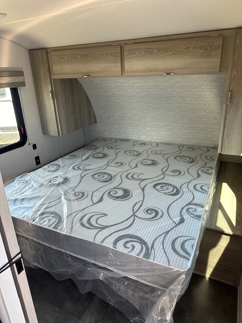 Inside this **RV rental** is a tidy bedroom with a new, plastic-covered mattress, overhead cabinets, and patterned headboard wall.. Forest River SALEM FSX 2024