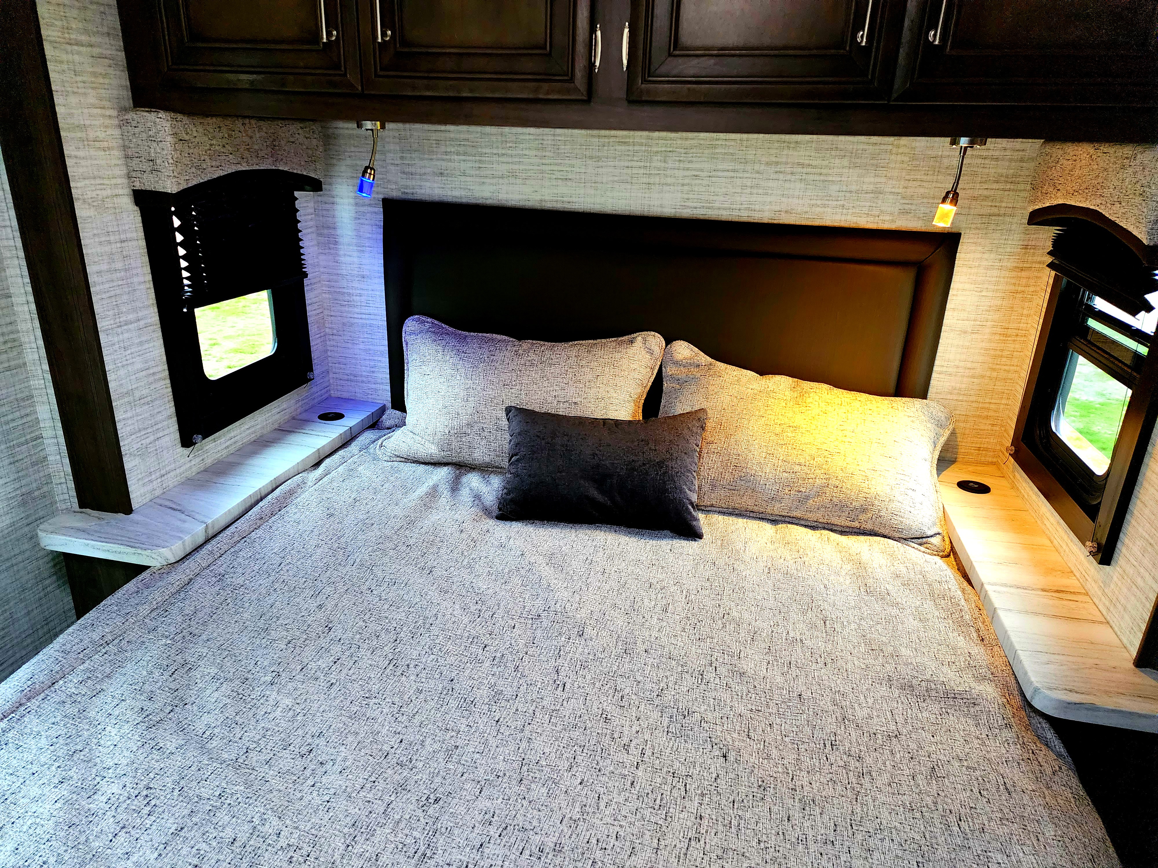 Inviting RV rental bedroom with bed, overhead cabinets, dual reading lights (blue & warm), and window views.. Jayco Entegra Odyssey 2024