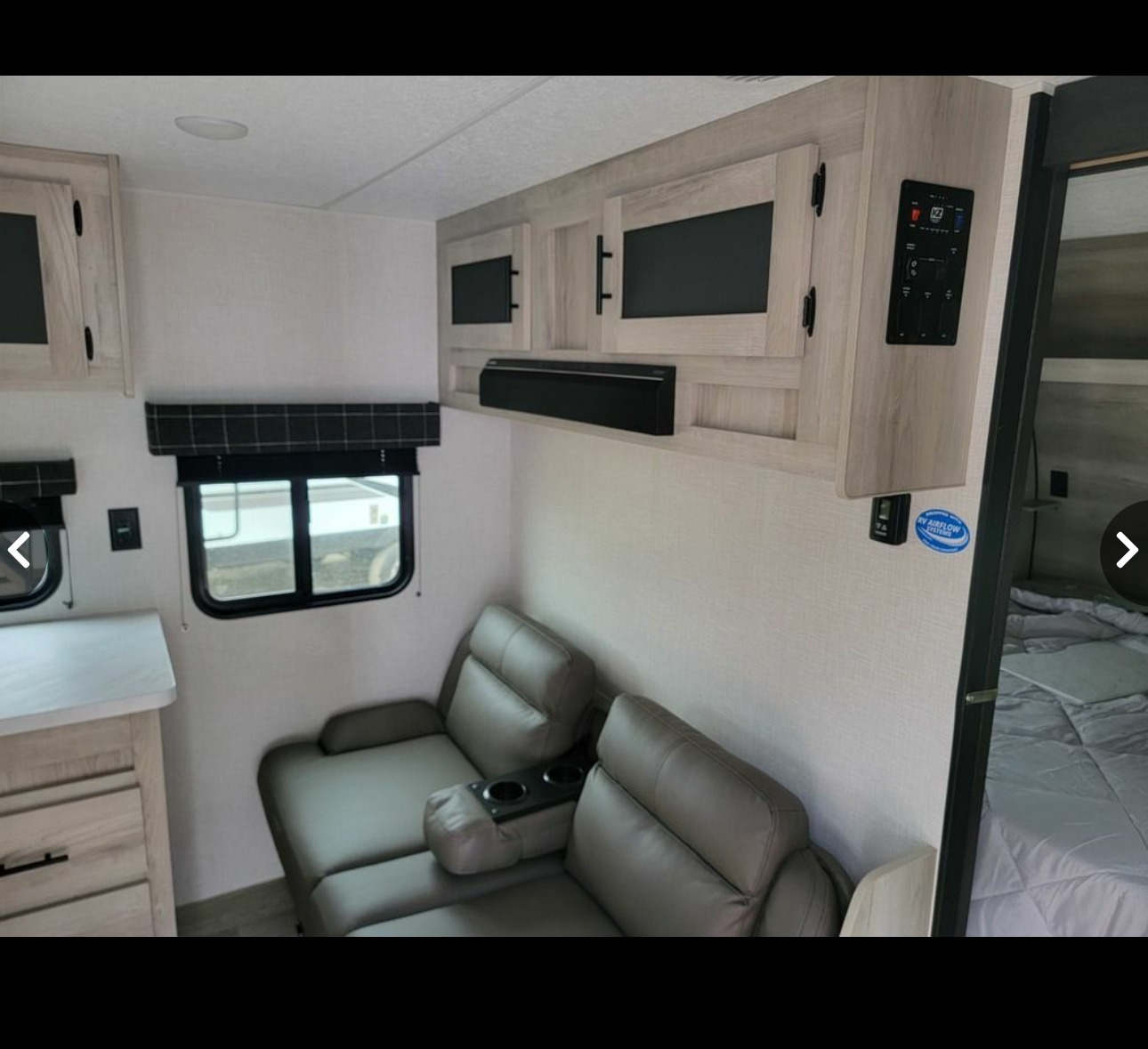 Inside this RV rental: light-toned cabinets, comfortable recliners with cupholders, windows, and a compact bedroom area.. Sportsmen SE 2023