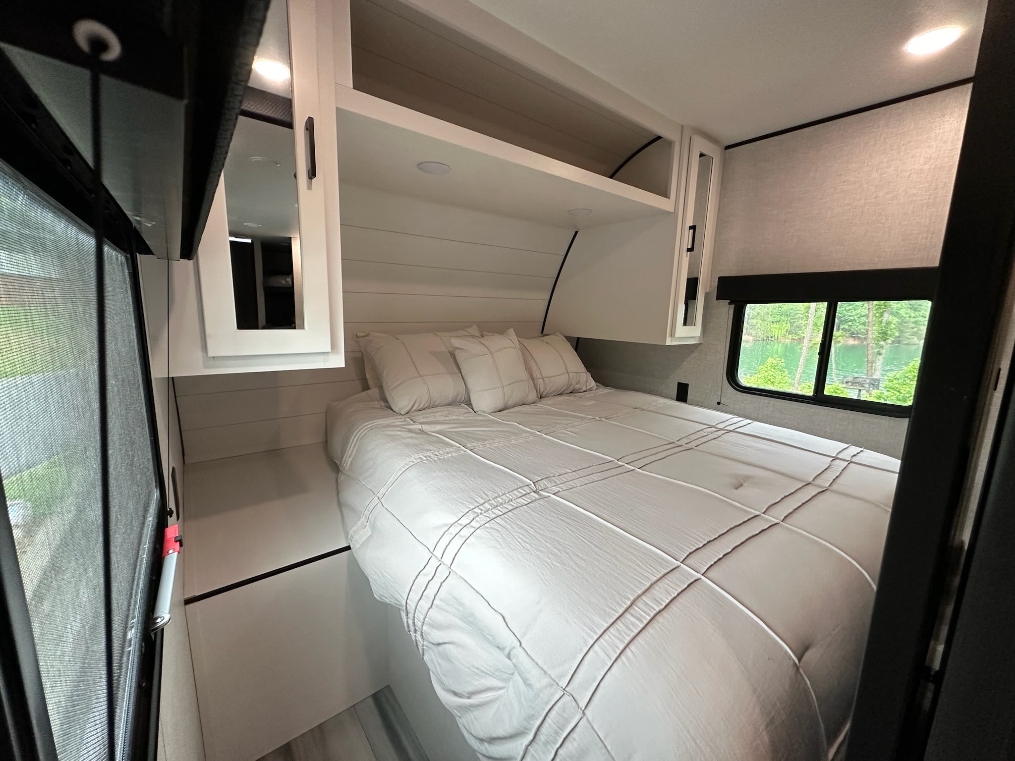 Bright RV rental bedroom showcasing a comfortable white bed, overhead storage, and a large window with a nature view.. Jayco Jay Flight SLX 2024