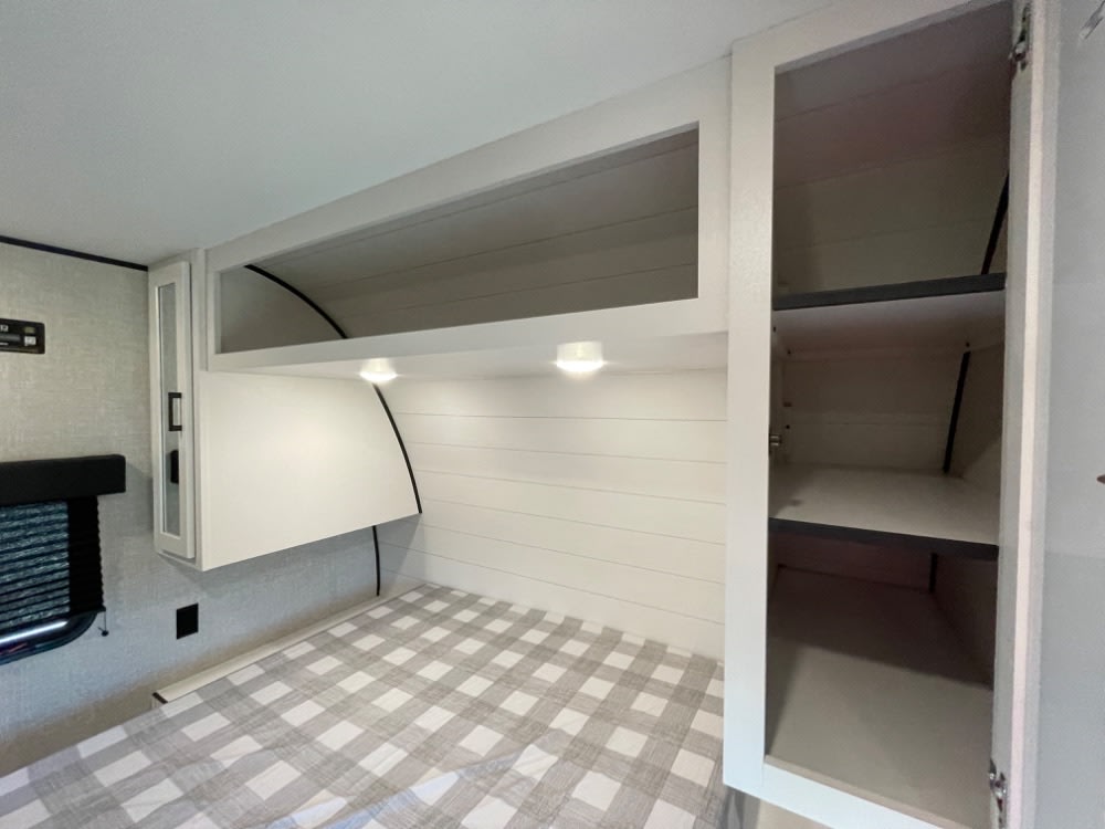 Cozy RV rental bedroom featuring a checkered bed, white overhead cabinets, task lighting, and shiplap-style wall.. Jayco Jay Flight SLX 2024