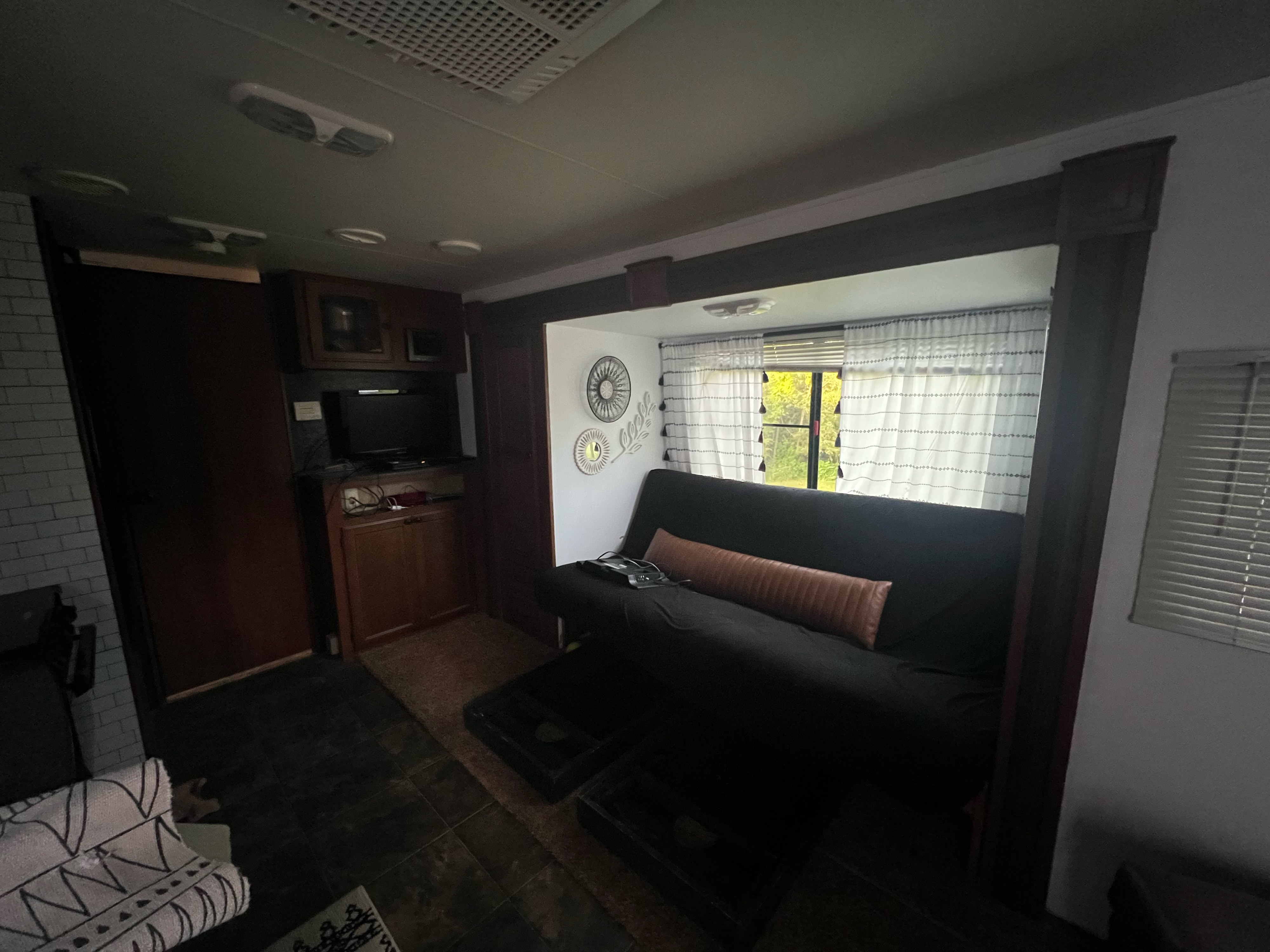 Step inside this cozy RV rental's living area, featuring a sofa, kitchen space with TV, and bright window with curtains.. Heartland RVs North Trail 2012