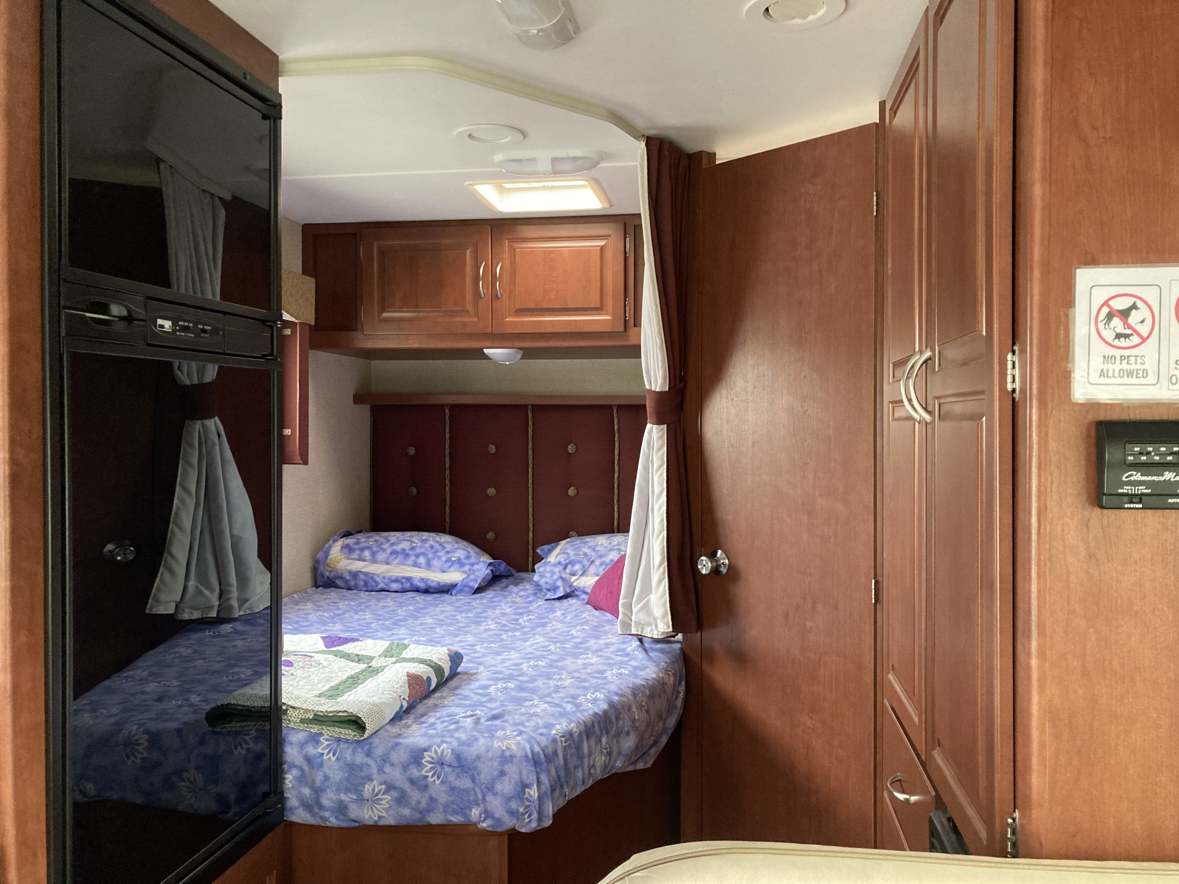 An RV rental's compact sleeping area, showing a bed, overhead cabinets, and a refrigerator.. Winnebago Minnie Winnie 2015