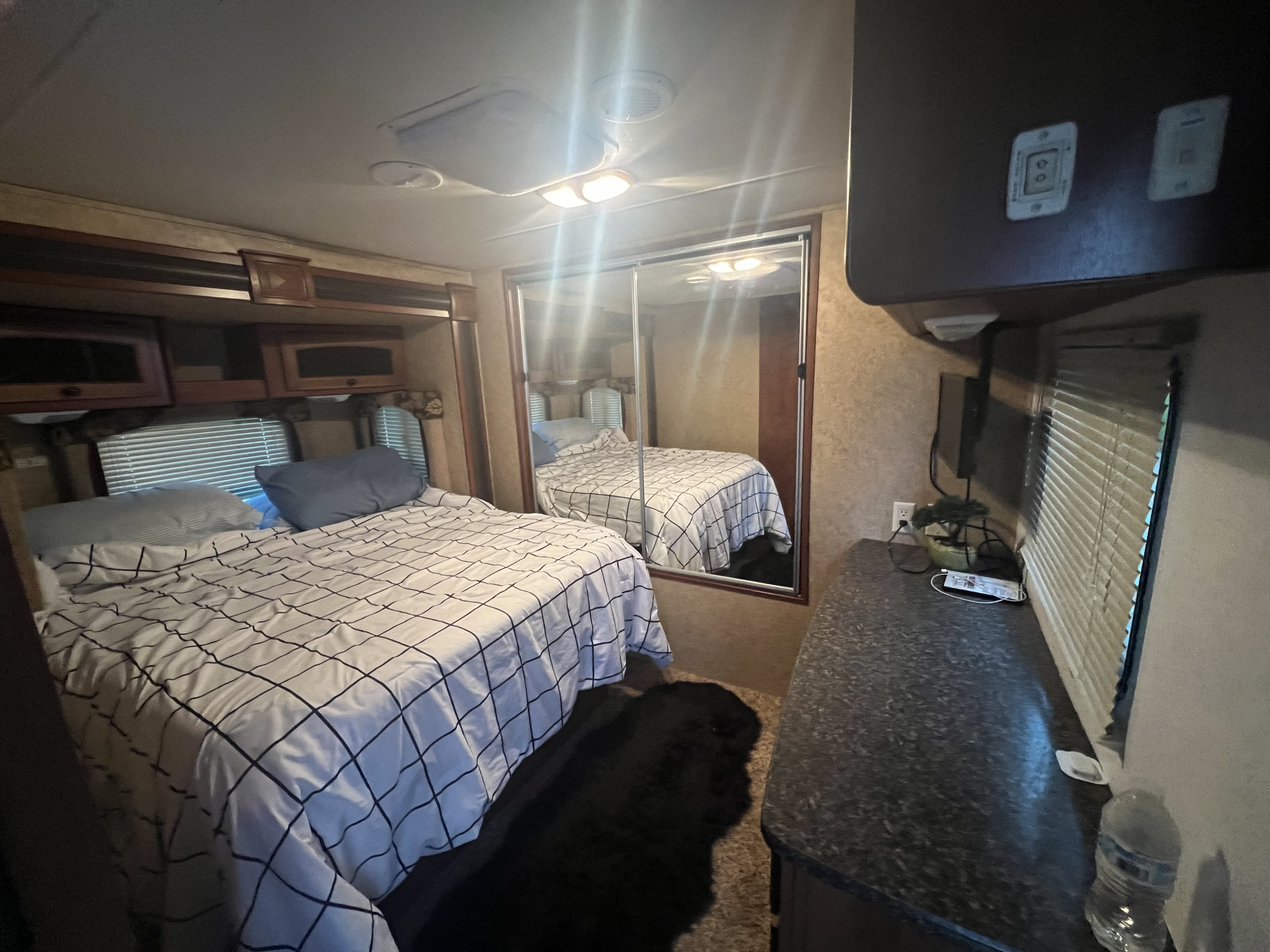 Inside a cozy RV rental bedroom: a comfortable bed, mirrored closet, cabinets, counter, and a furry black dog.. Heartland RVs North Trail 2012