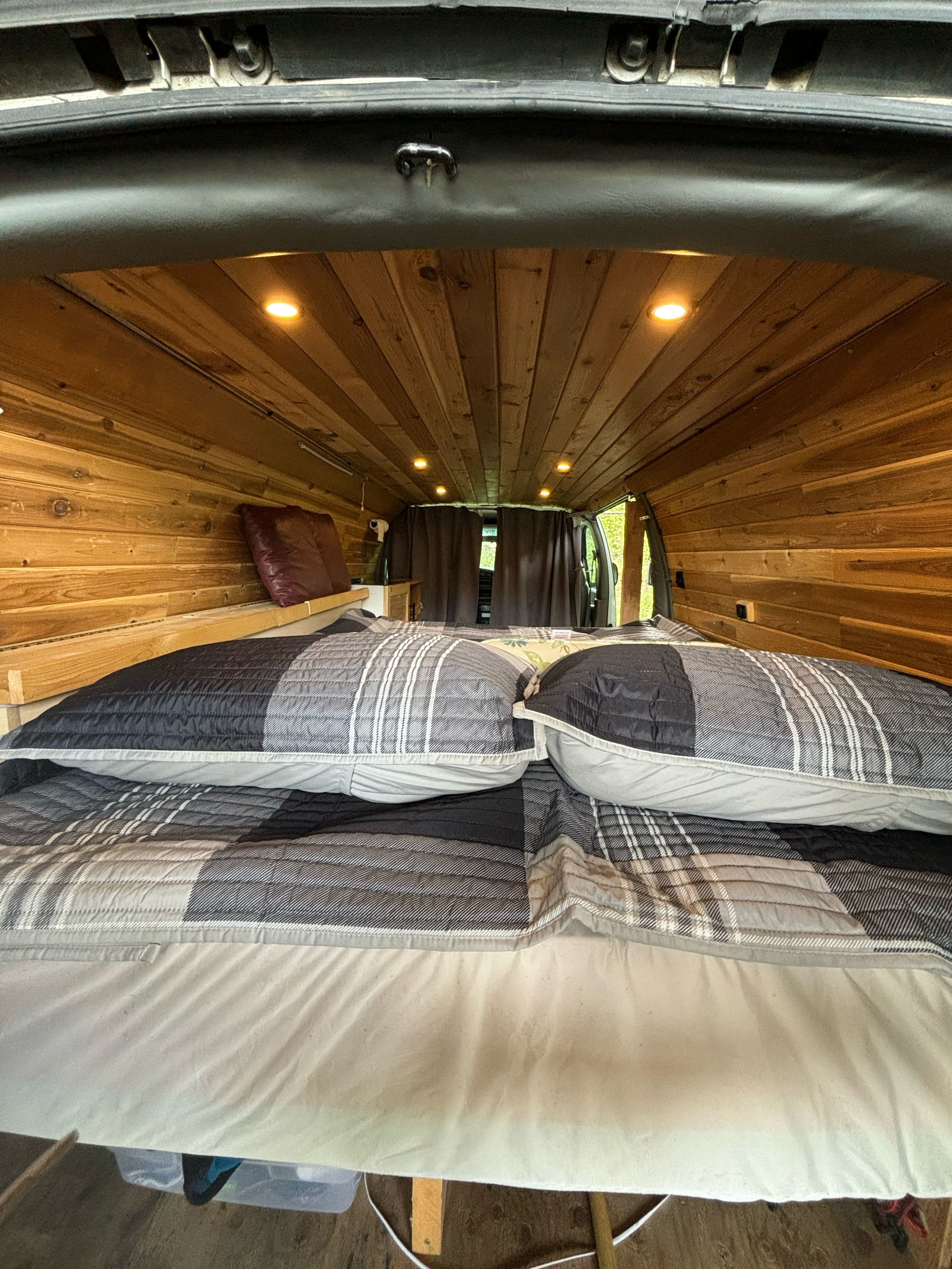 Inside this RV rental camper van: a cozy bed with plaid bedding, wood-paneled walls, and warm ceiling lights.. Gmc Savanna 2000