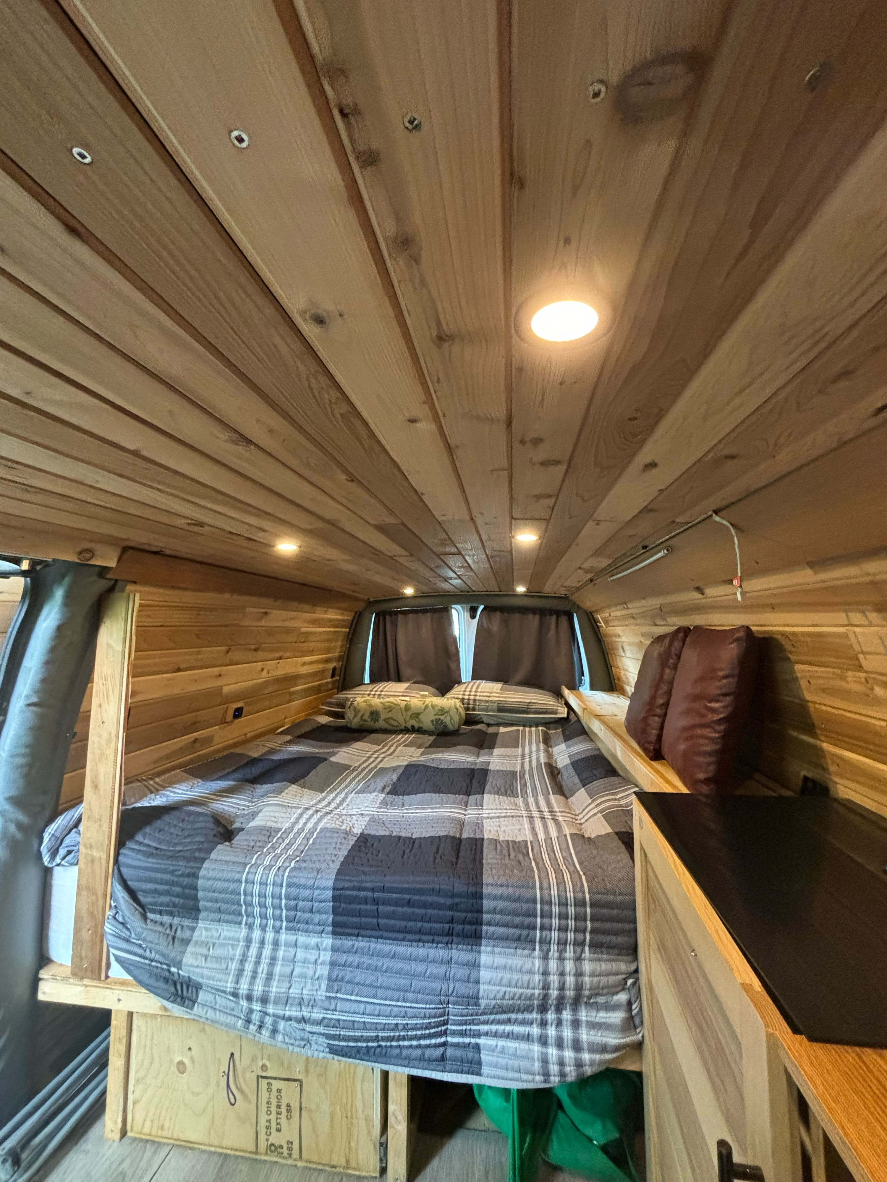 Cozy RV rental interior: custom wood paneling, bright recessed lights, and a comfortable plaid bed.. Gmc Savanna 2000
