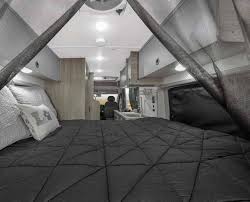 Spacious RV rental interior: Dark bed in foreground, light cabinets & kitchen lead to driver area.. Winnebago Winnebago 2023
