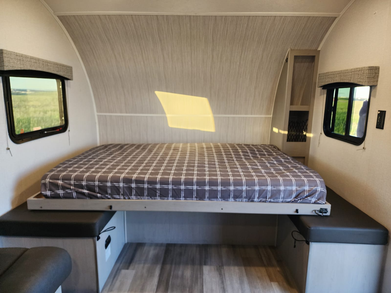 Plaid bed with side benches in a compact RV rental bedroom. Windows offer scenic views, plus built-in storage on the right.. Forest River Coachmen Classic 2023