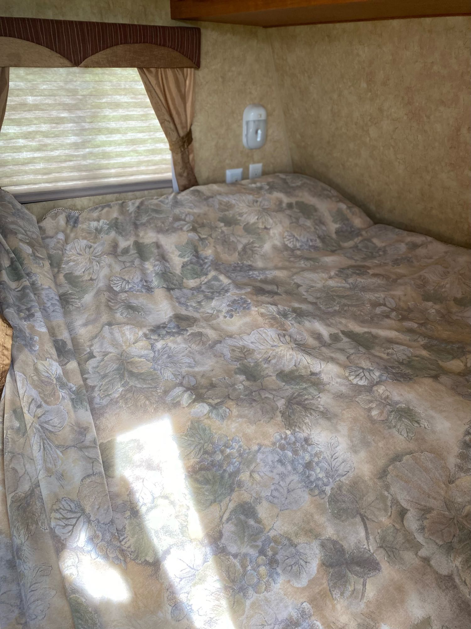 Cozy RV rental bedroom with floral comforter, window blinds, and wall light. Ideal for a comfortable travel stay.. Starcraft Autumn Ridge 2011