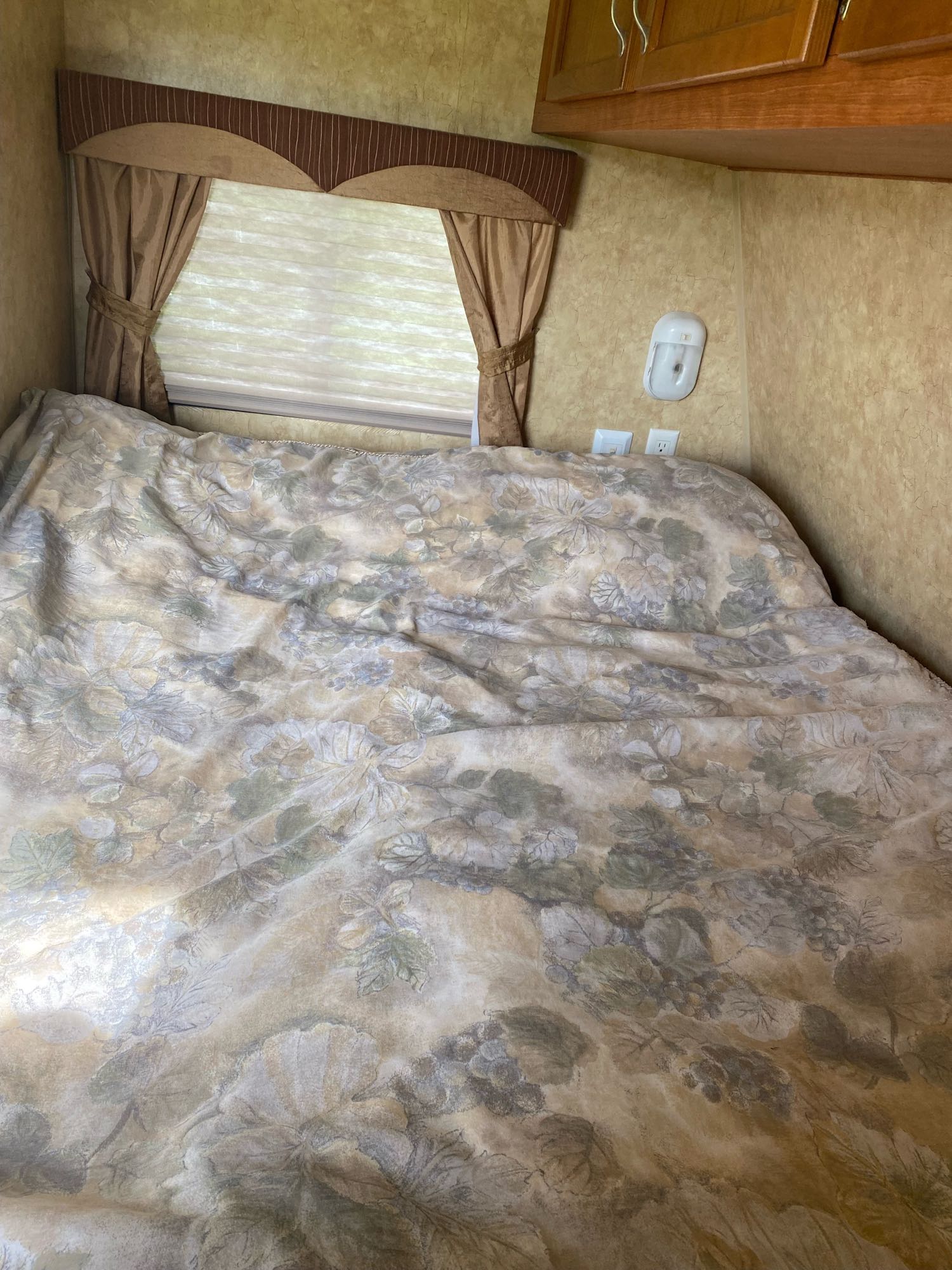 Cozy RV rental bedroom featuring a floral bed, window with curtains, and wall outlets.. Starcraft Autumn Ridge 2011