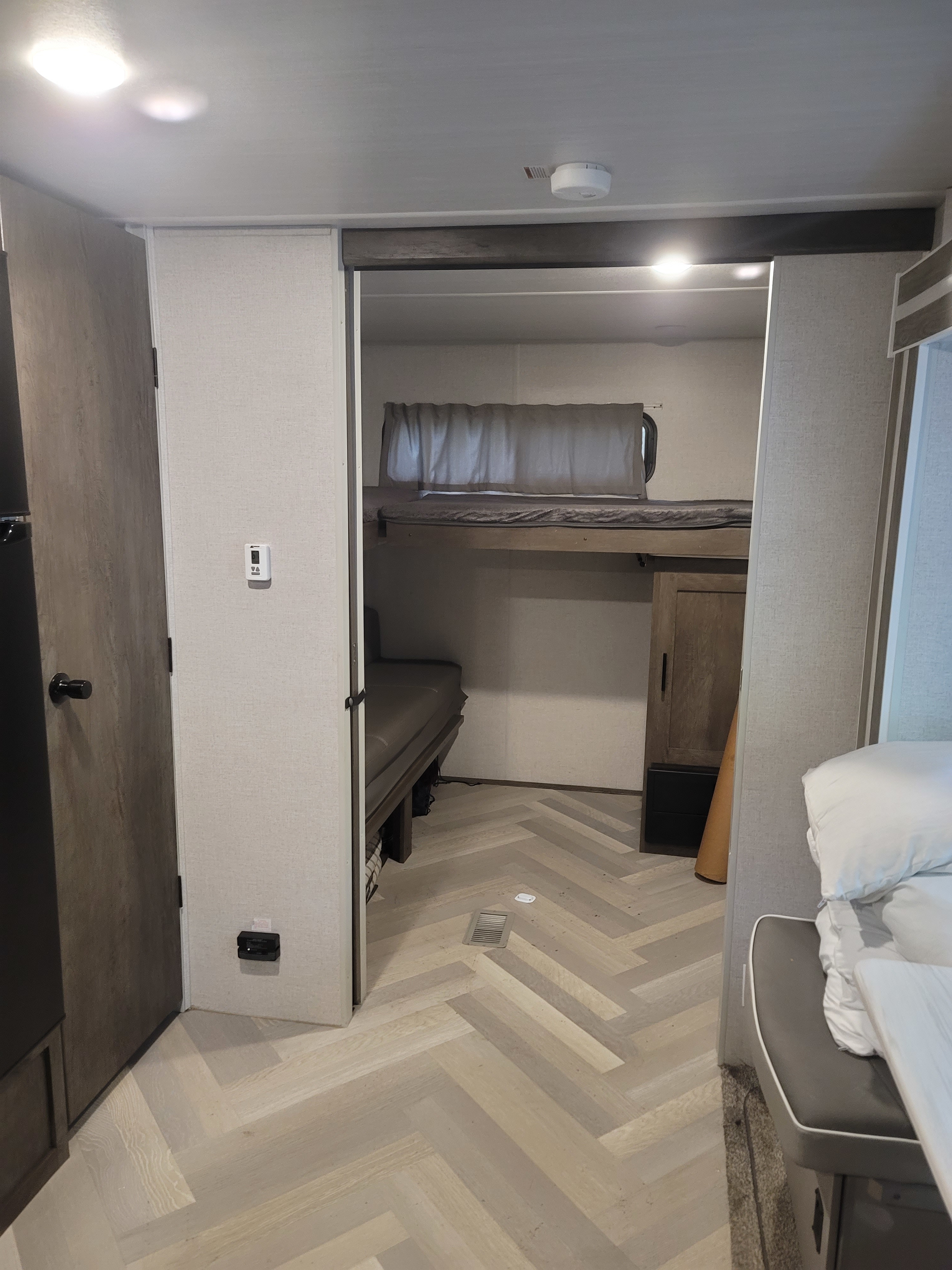 RV rental interior: Light herringbone flooring leads to a bunk room with two beds. A smoke detector and wall thermostat are visible.. Forest River Salem 2021