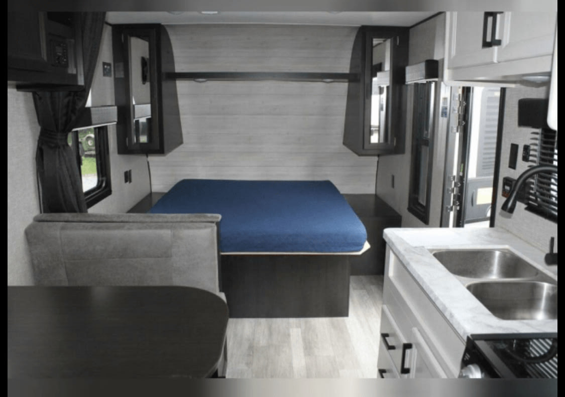 Interior of an RV rental showing a bed, dining booth with table, and a kitchen with double sink.. Jayco Jay Flight 2023