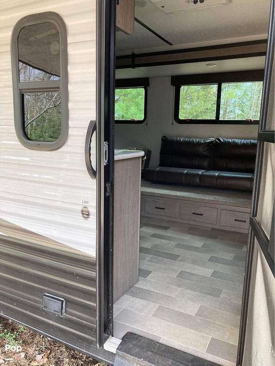 RV rental interior showing a cozy living space with a black sofa, windows, and light wood-look flooring.. Keystone RV Hideout 2023