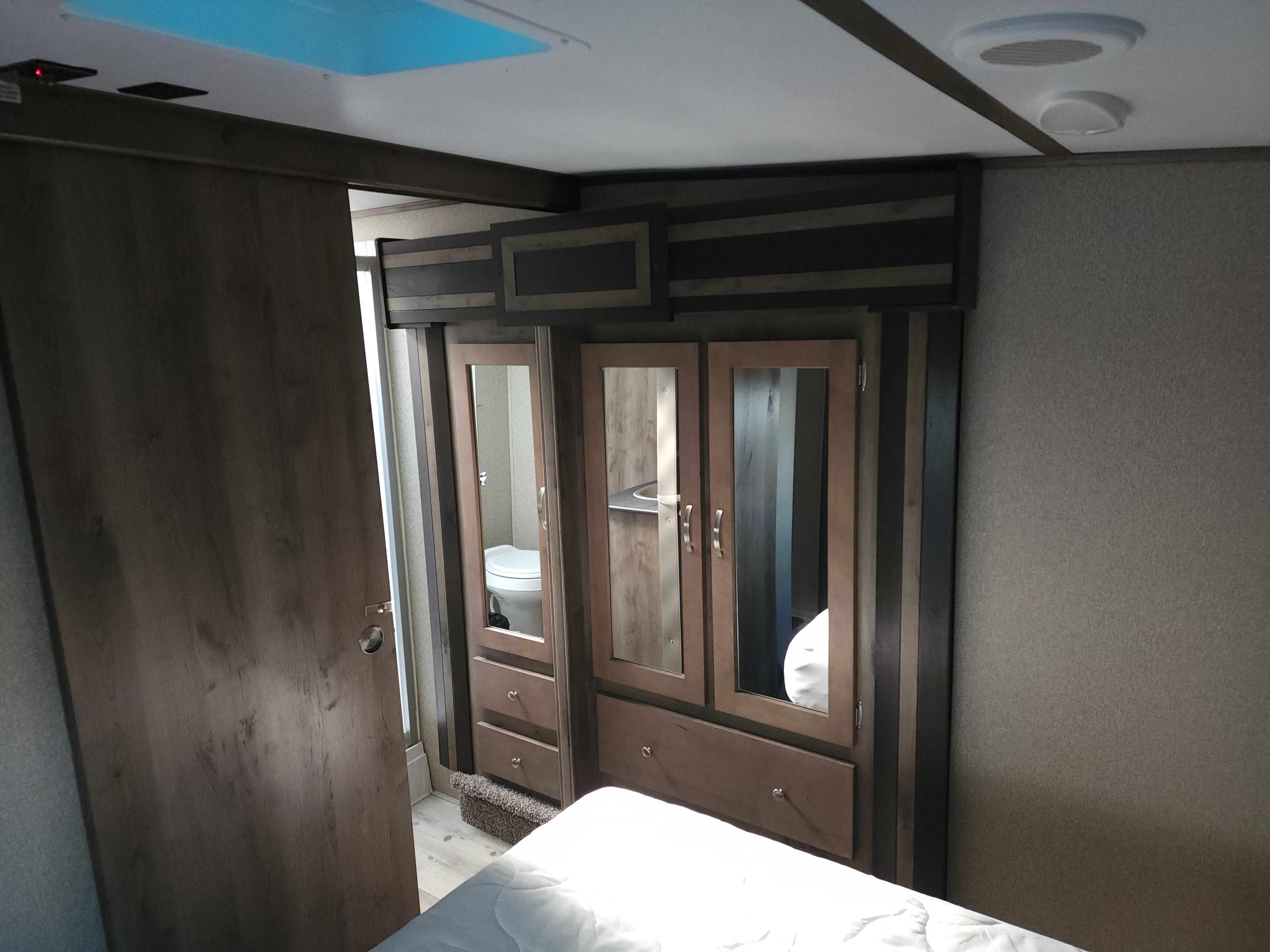 RV rental bedroom featuring a wooden wardrobe with mirrors & sliding door to a private bathroom.. Keystone RV Sprinter Campfire Edition 2019