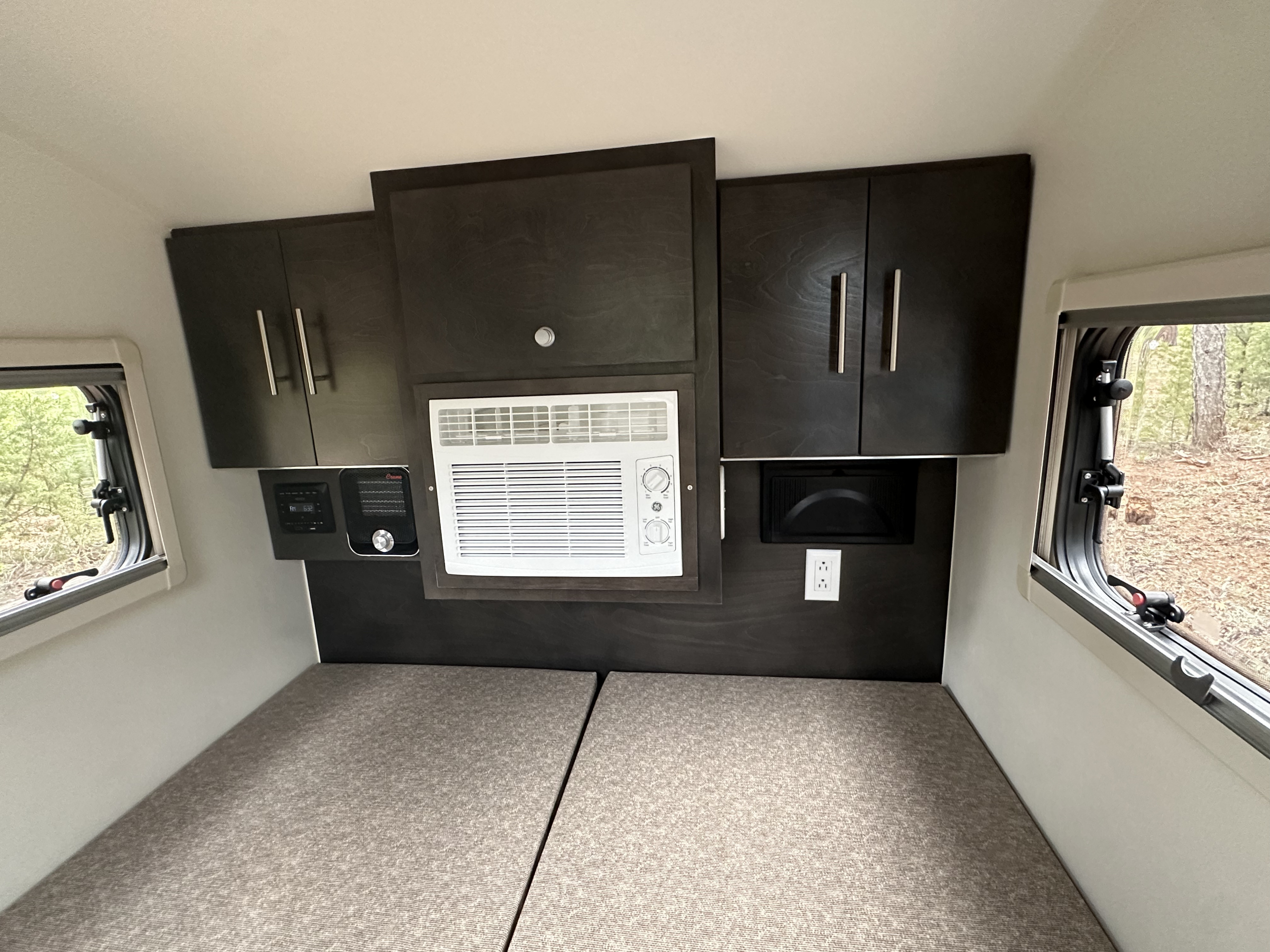 Cozy RV rental interior featuring convertible beds, dark cabinets, an AC unit, and scenic windows for comfortable camping.. nuCamp T@G 2021