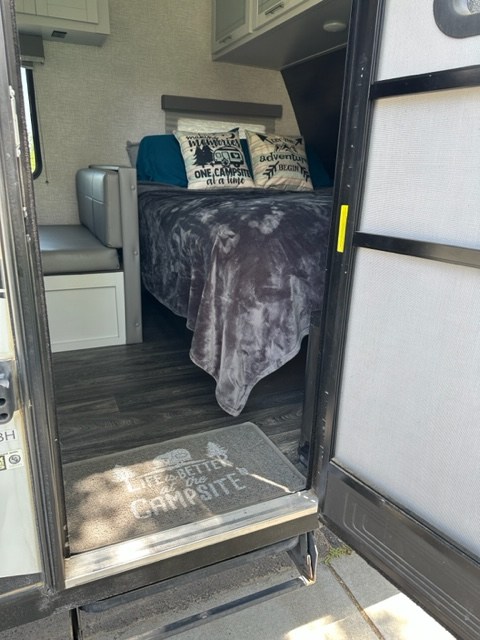 This comfortable RV rental interior shows a bed with pillows, a bench, and a "Life is Better at the Campsite" mat.. Keystone RV Bullet Crossfire 2021
