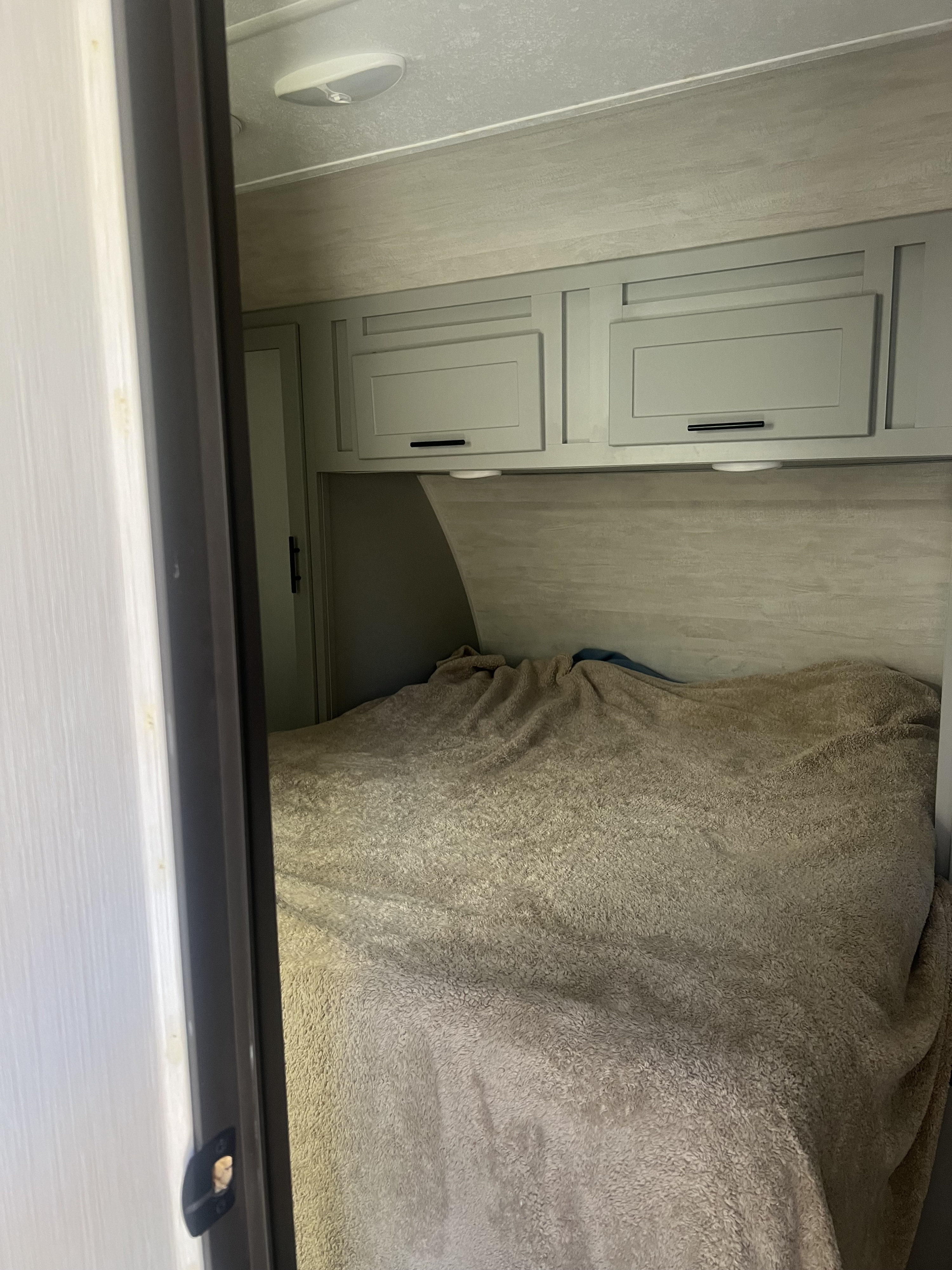 Cozy RV rental bedroom with a comfortable bed, overhead cabinets, and bright ceiling light, offering a snug space for travel.. Forest River Vibe 2021