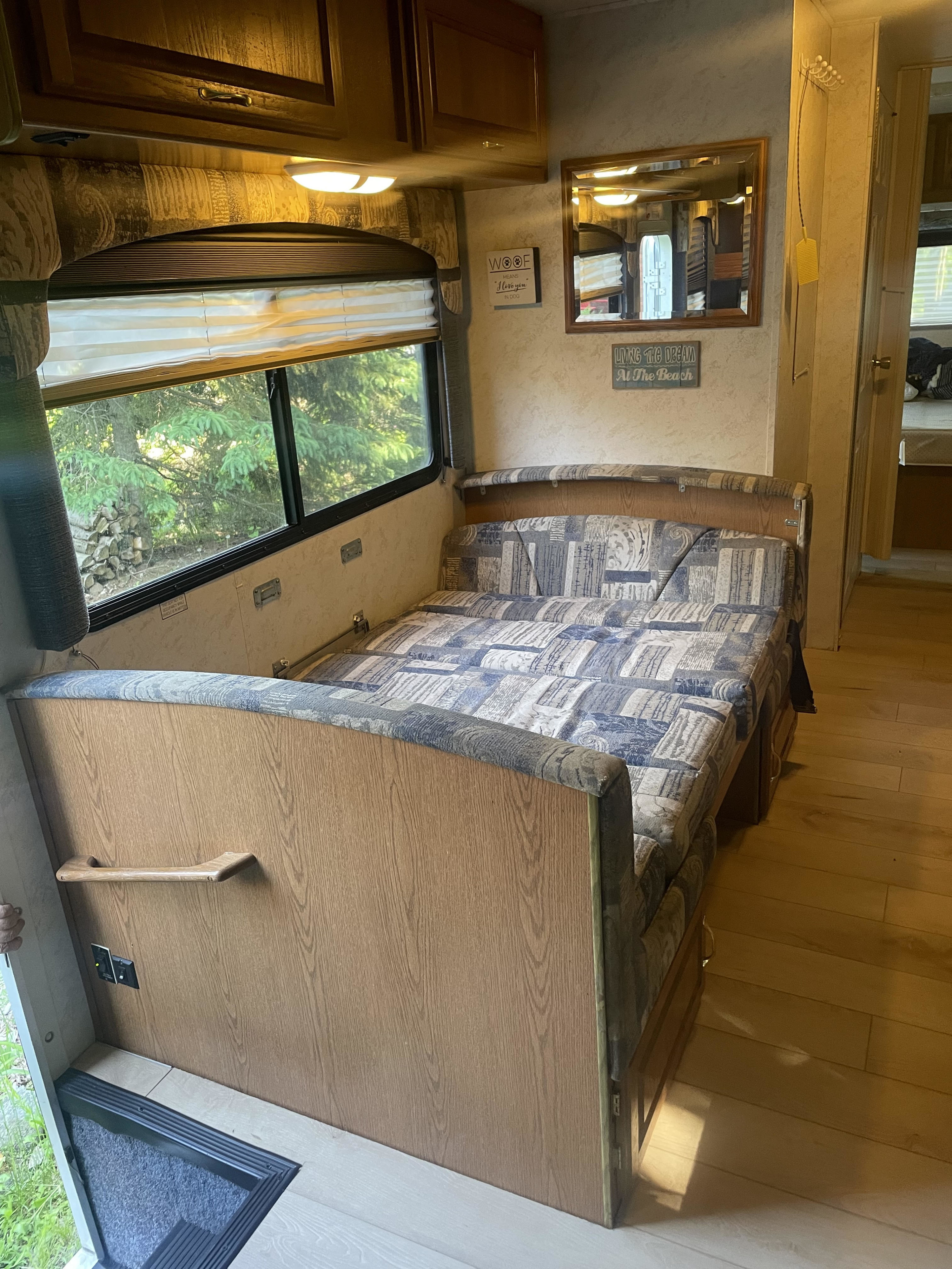 Cozy RV rental interior: convertible bed, large window with nature view, wood-look floor, and storage cabinets.. Four Winds 5000 2002
