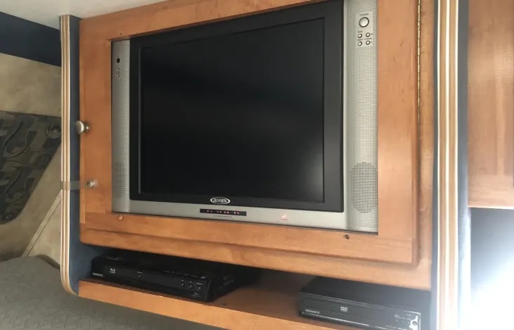 Inside an RV rental: a built-in TV, Blu-ray, and DVD player setup within a wooden entertainment cabinet.. Gulf Stream RV 6237 2008