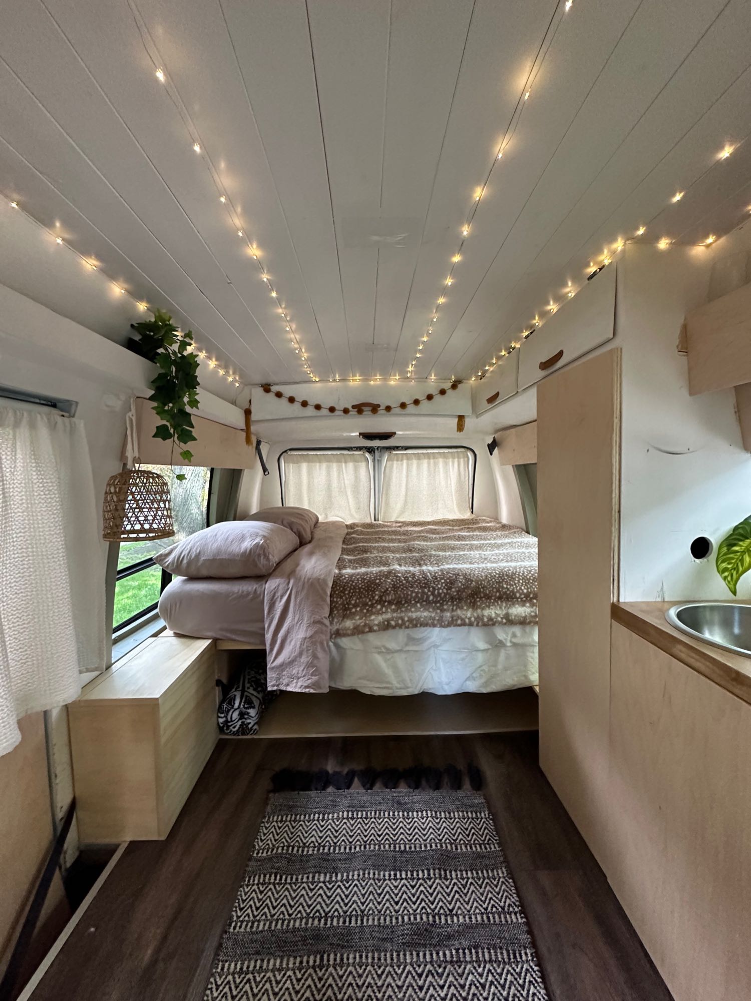 Cozy camper van interior, available for rv rental. Features a comfortable bed, string lights, and compact kitchen.. GMC Vandura 2500 1992