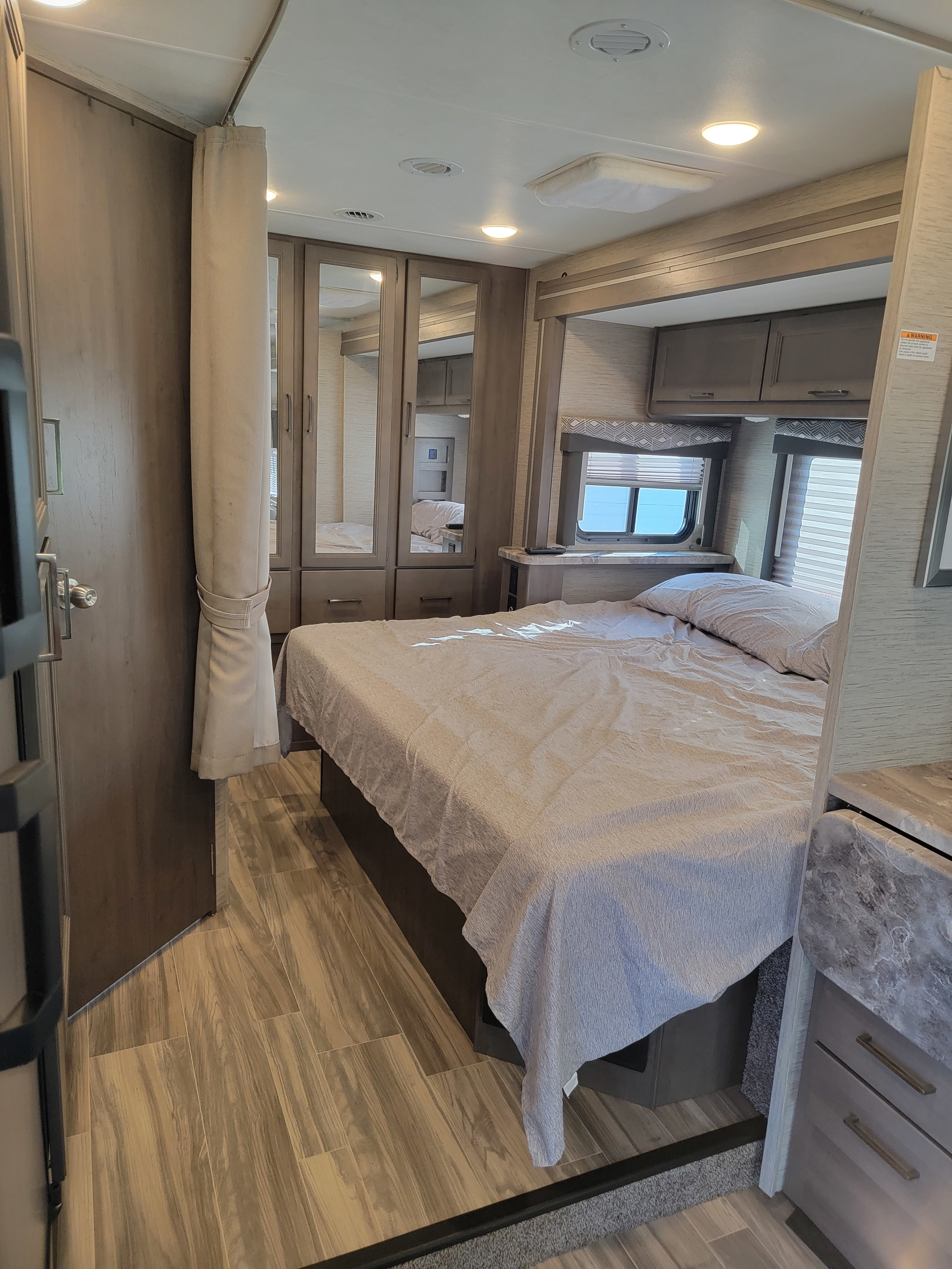 Spacious RV rental bedroom, featuring a large bed, built-in storage with mirrored closets, and wood-look flooring.. Thor Four Winds 2023