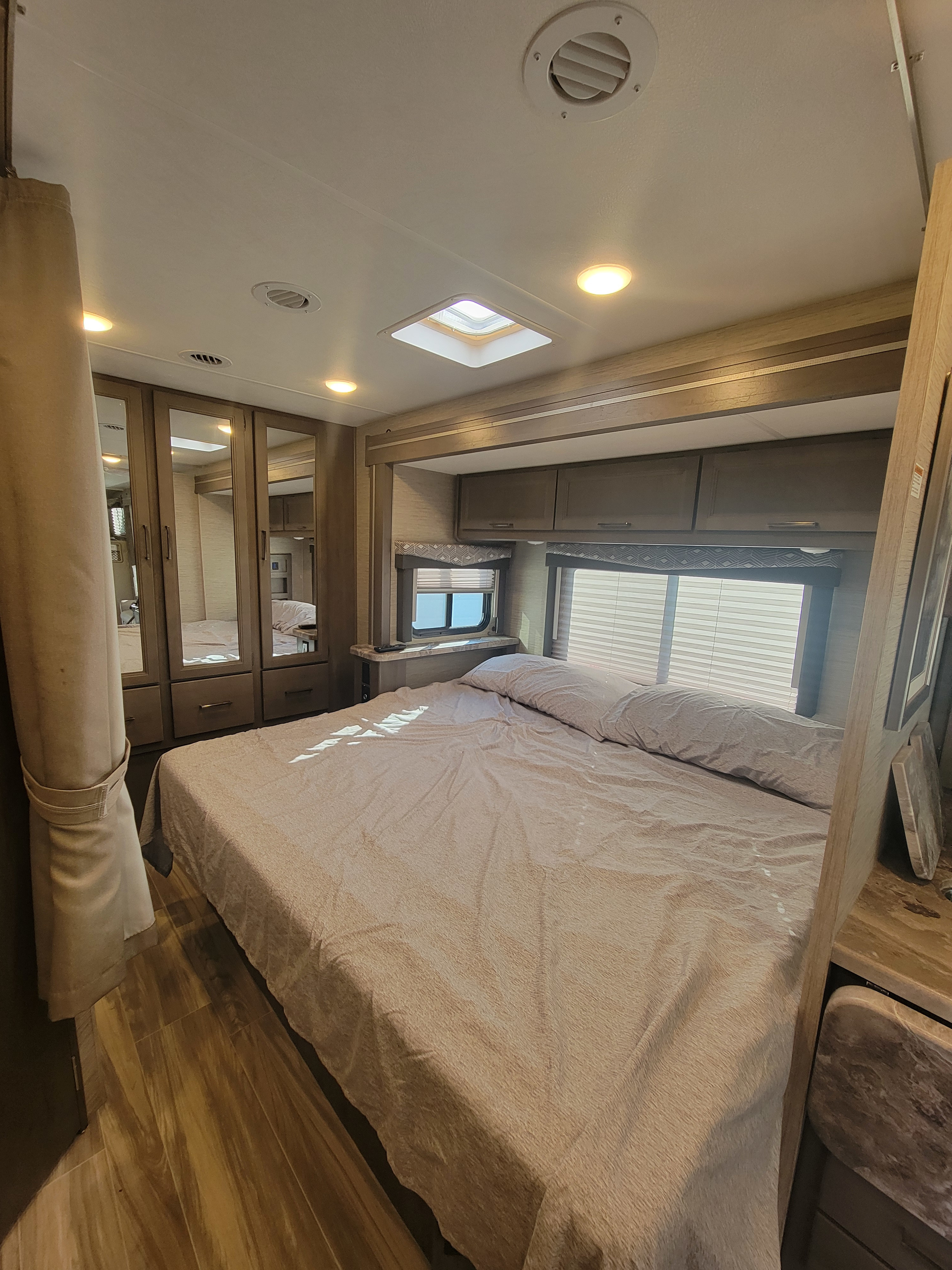 Comfortable RV rental bedroom showing a bed, mirrored storage, skylight, and bright windows.. Thor Four Winds 2023