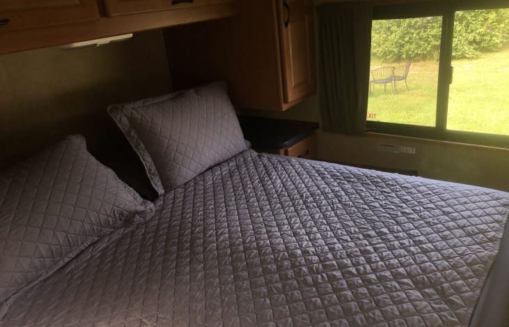Cozy RV rental bedroom featuring a comfortable bed, overhead cabinets, and a window with an outdoor view.. Thor Majestic 2016