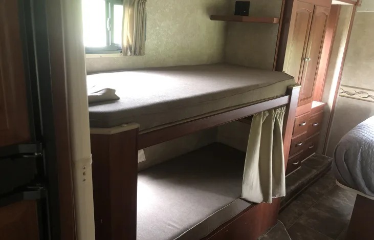 Cozy RV rental interior with bunk beds, a window, and storage cabinets, ideal for family adventures on the road.. Winnebago Chalet 2014
